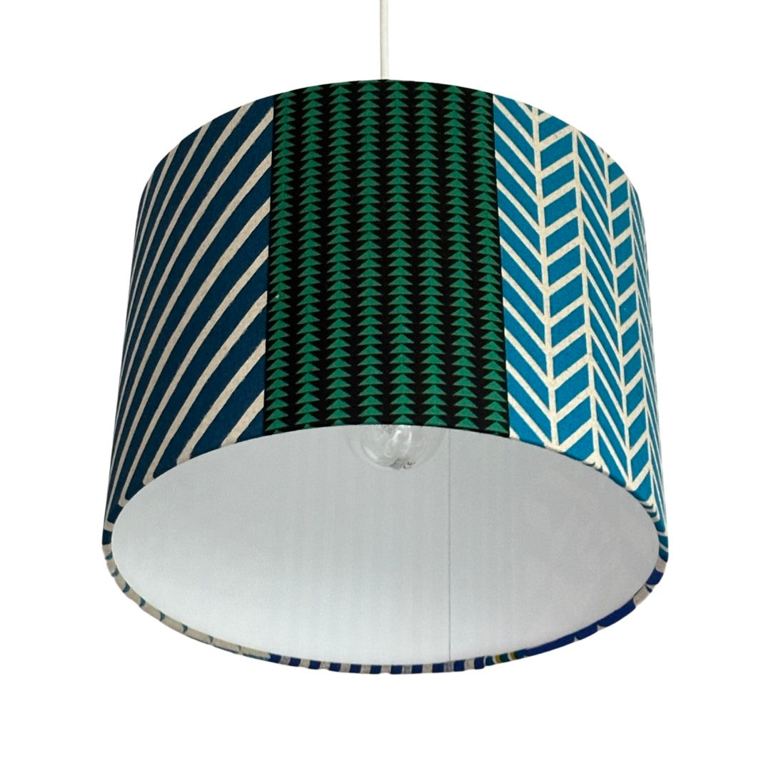 Close up of a drum lampshade in panels of blue, grey, green and grey geometric designs