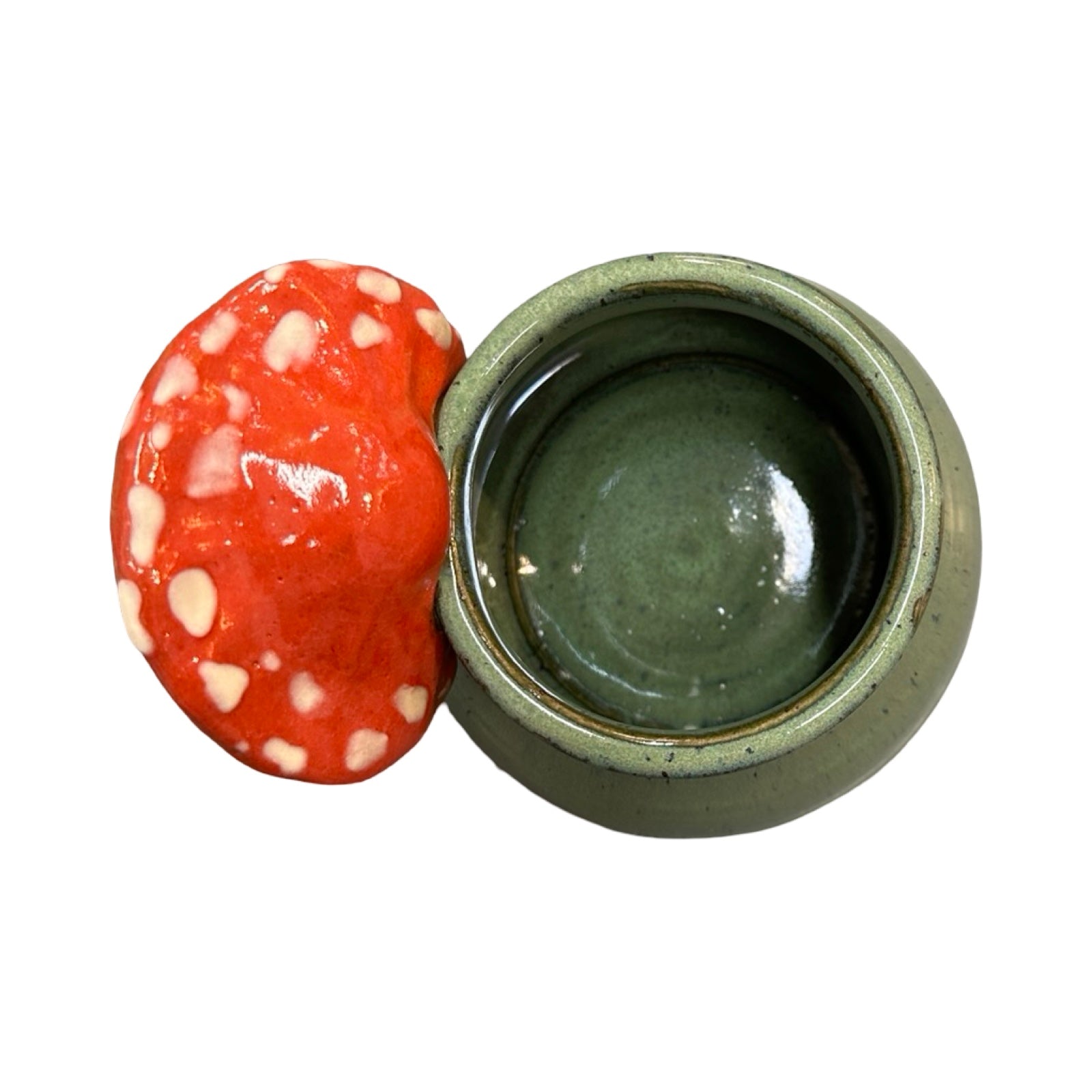 Ceramic mug with a red and white mushroom handle on a white background.