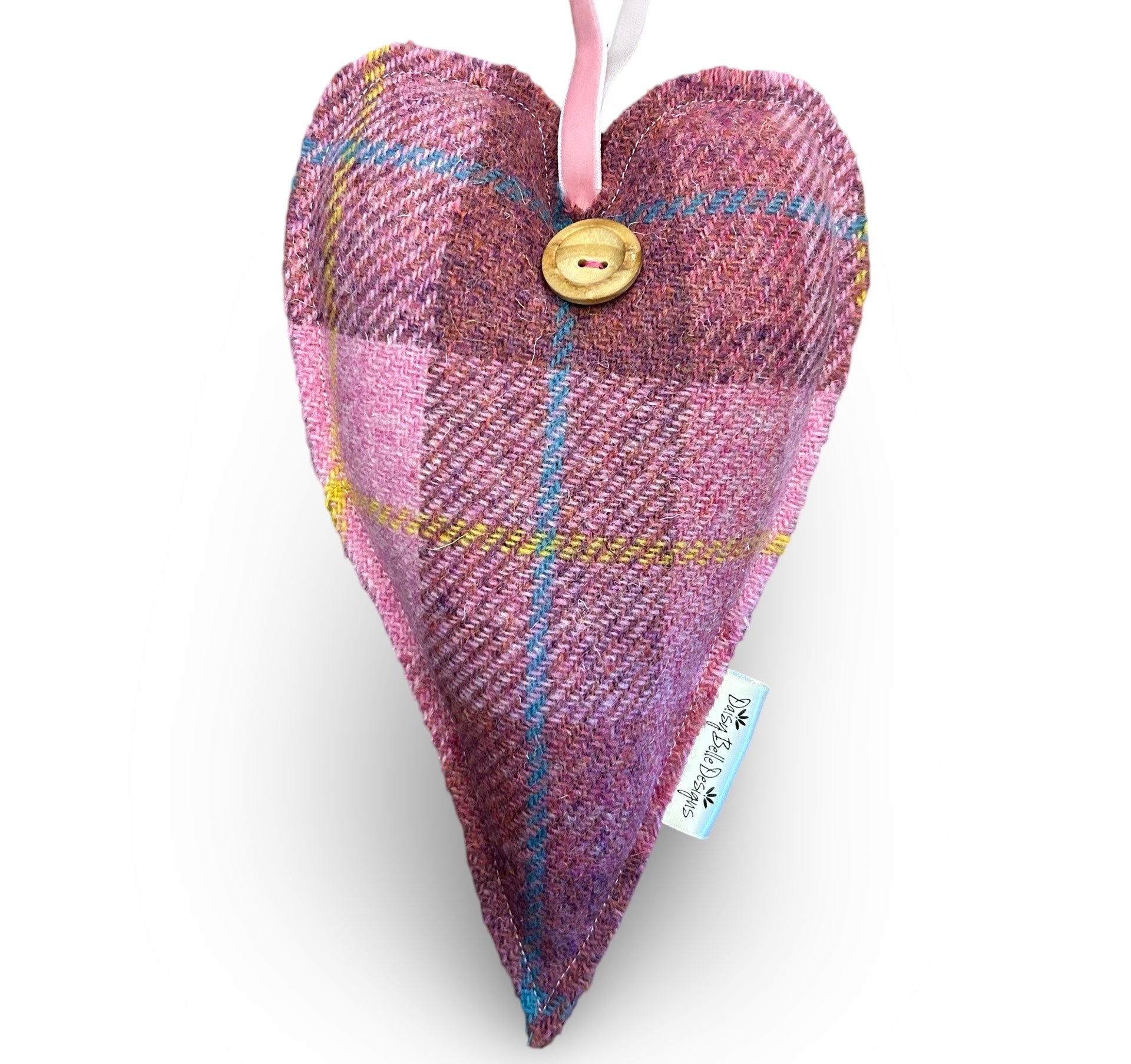 Large Harris tweed heart in pink tartan style wool tweed. The heart has a wooden button and pink velvet ribbon loop. There is a Daisy Belle Designs label in the side seam.