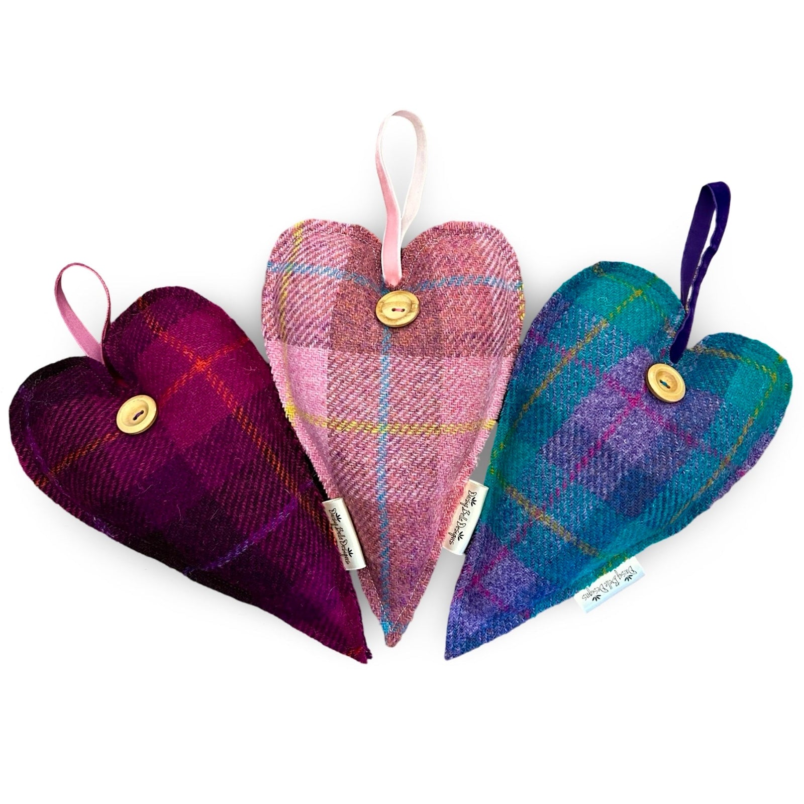 Three large Harris tweed lavender hearts each with a wooden button and a velvet ribbon loop at the top. One is cerise and purple, one is pink and the other is turquoise and lilac.
