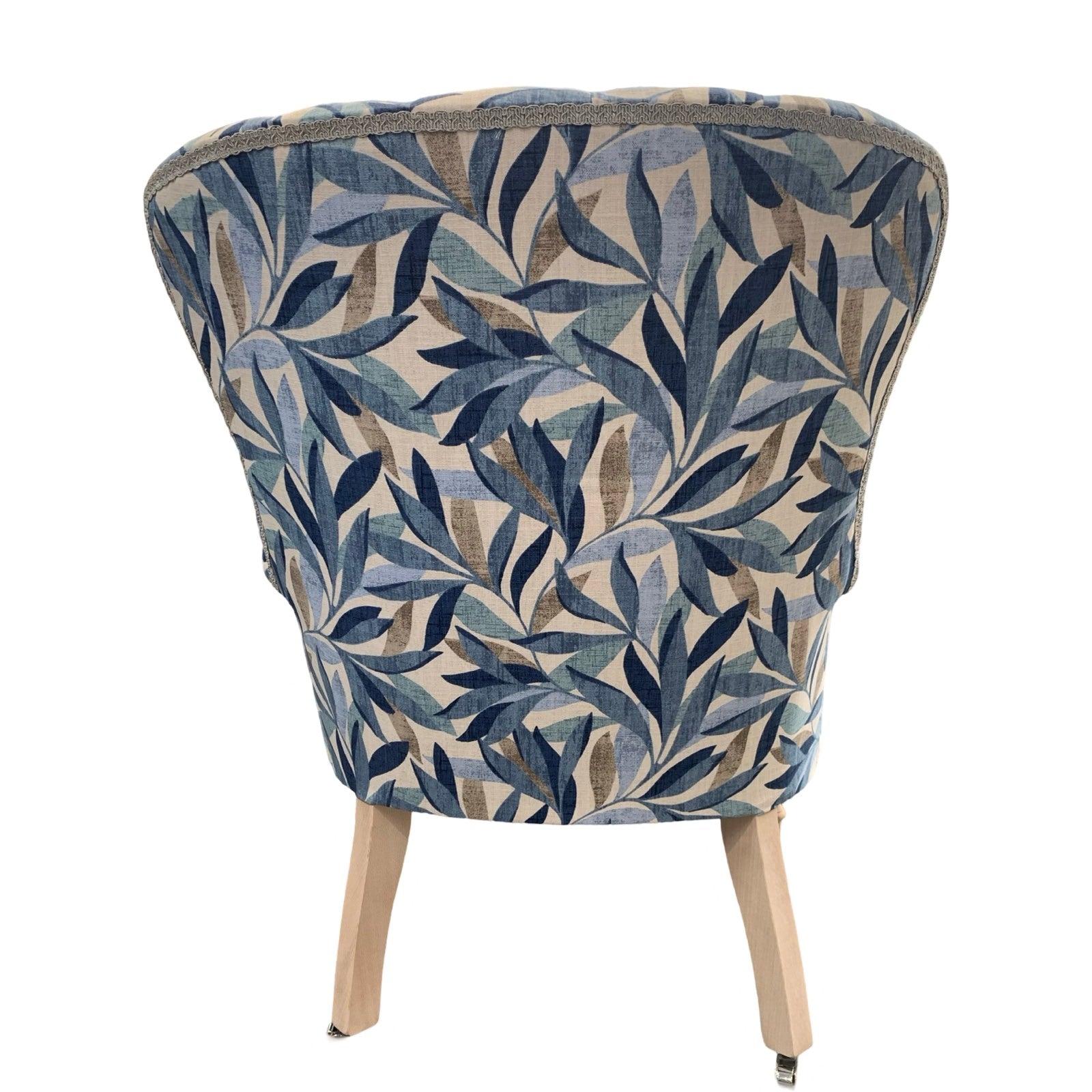 A blue linen armchair with a leaves pattern, featuring button-back tufting and oak legs with gold castors.