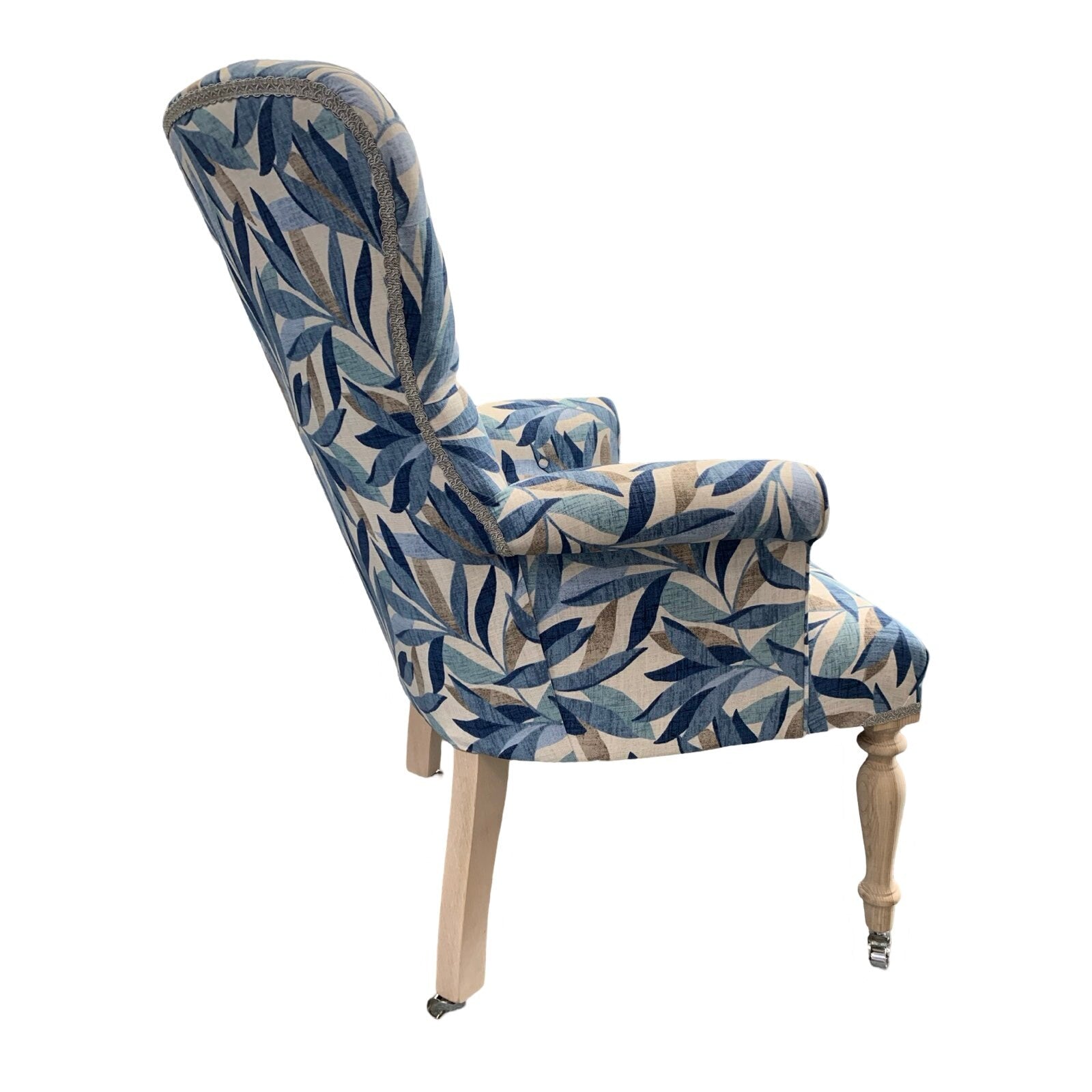 A blue linen armchair with a leaves pattern, featuring button-back tufting and oak legs with gold castors.