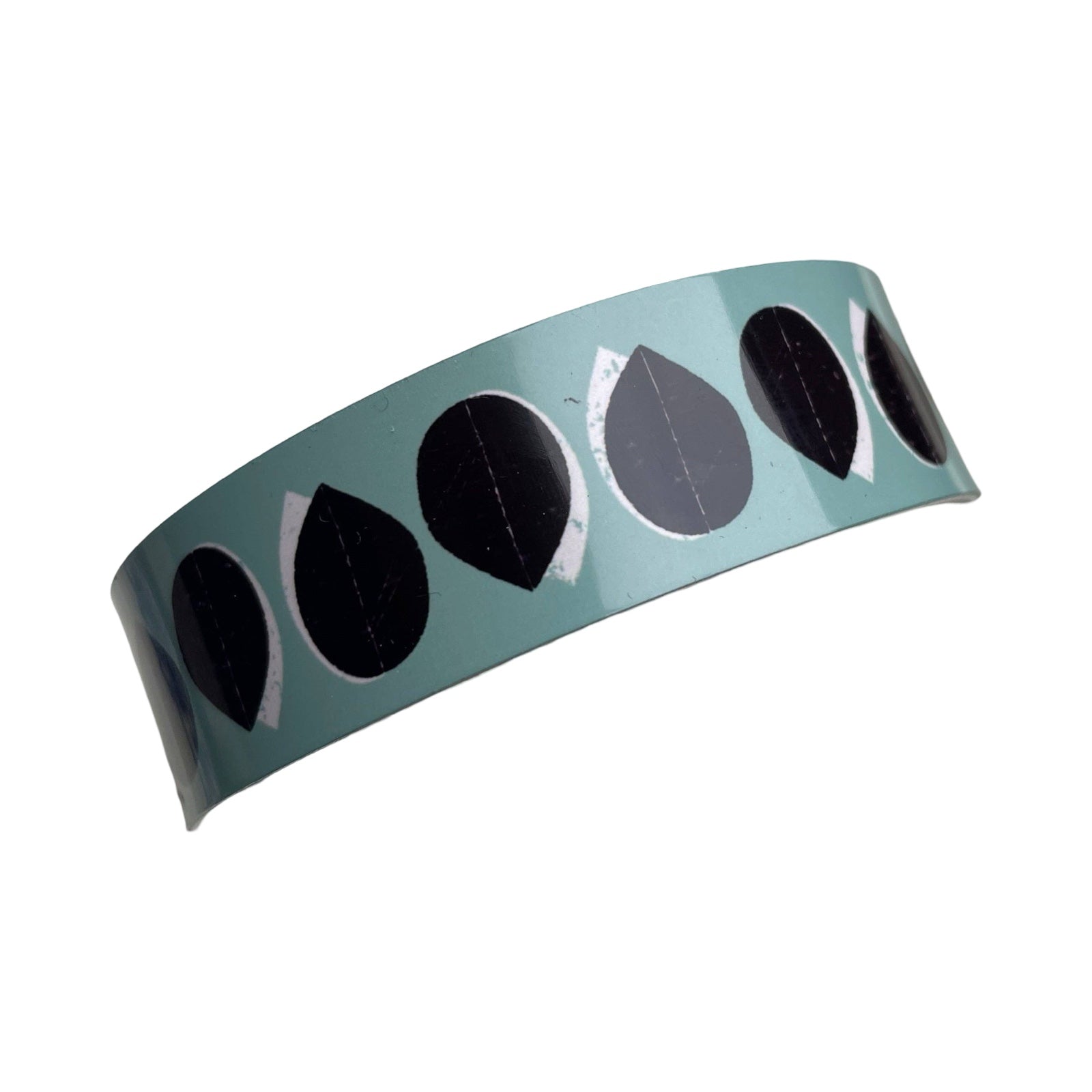 Narrow statement cuff bracelet featuring a black and white leaf-shaped design on a teal background.