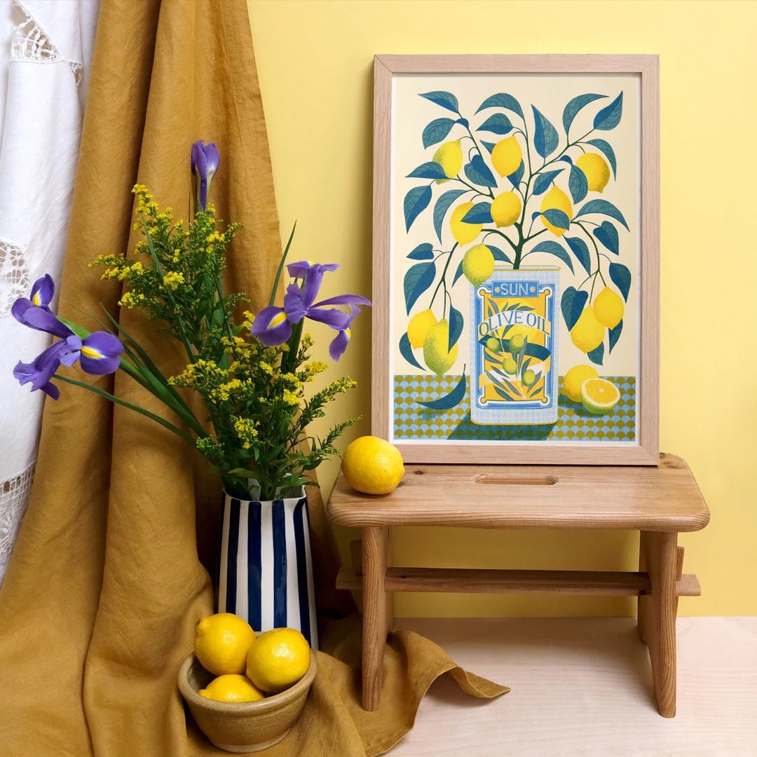 Framed artwork of lemons and a jar on a wooden stool with lemons and flowers in the foreground.