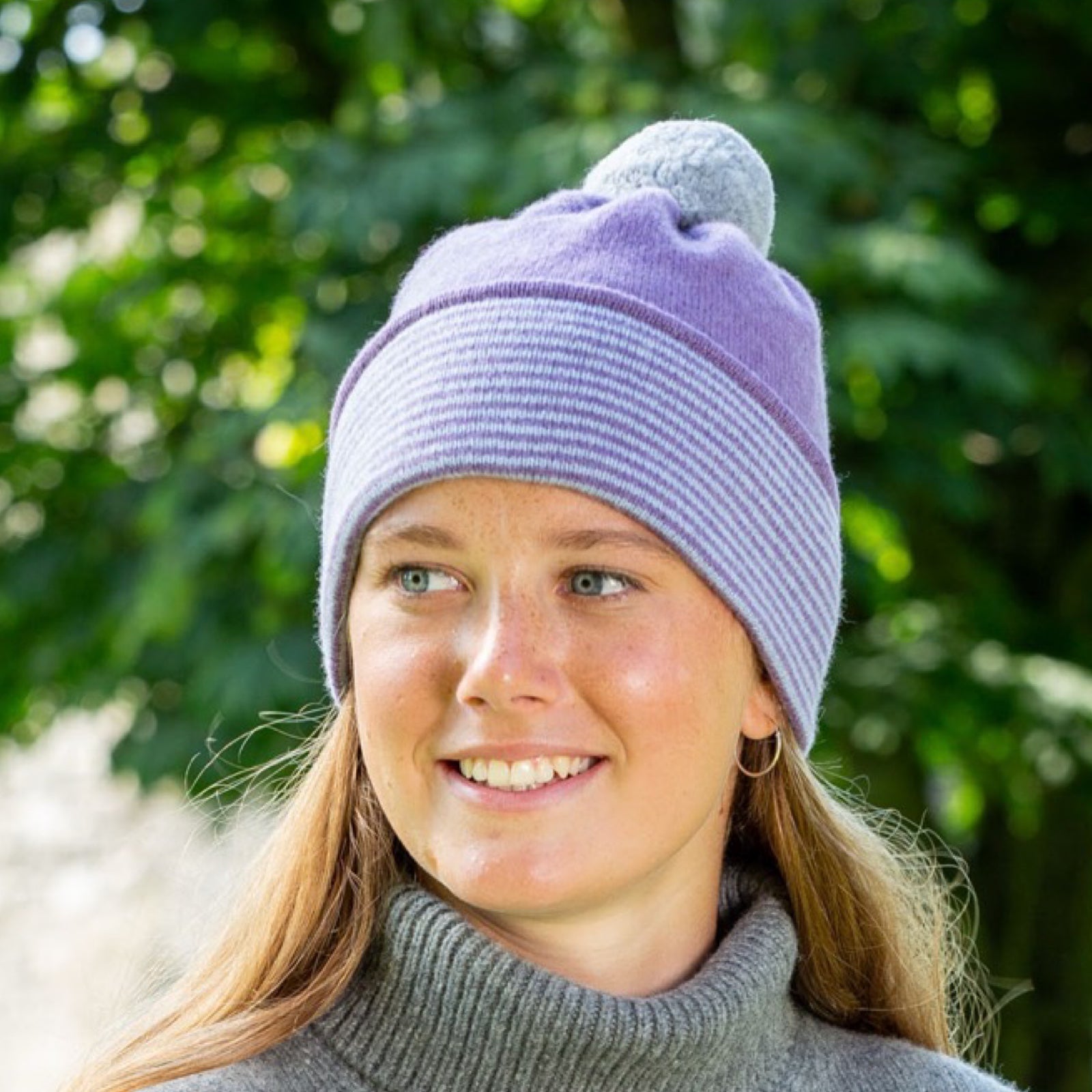 Person wearing a two-tone beanie with a fluffy top against a green leafy background.