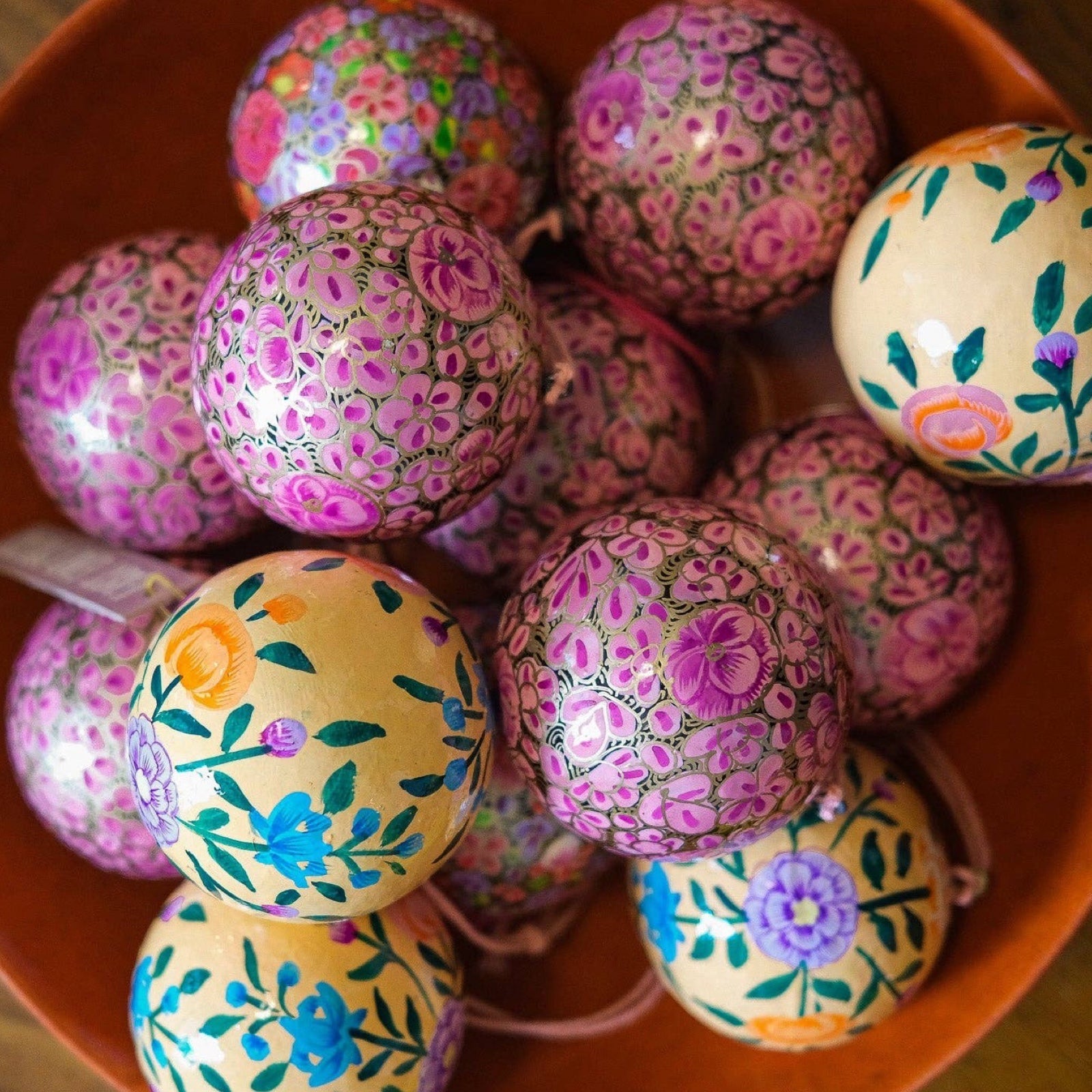 A bowl of lilac floral baubles and peach floral baubles.