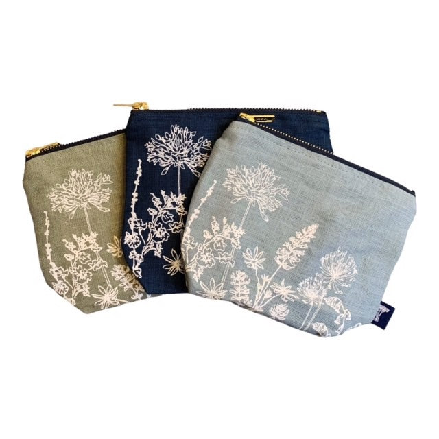 Three screen-printed linen make-up bags in navy, sage green, and duck egg blue with a floral design and a brass zip.