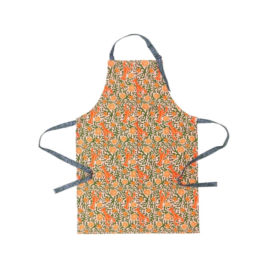 Pink and red apron featuring a lobster design, red lobsters and shells with green seaweed all on a pink background.