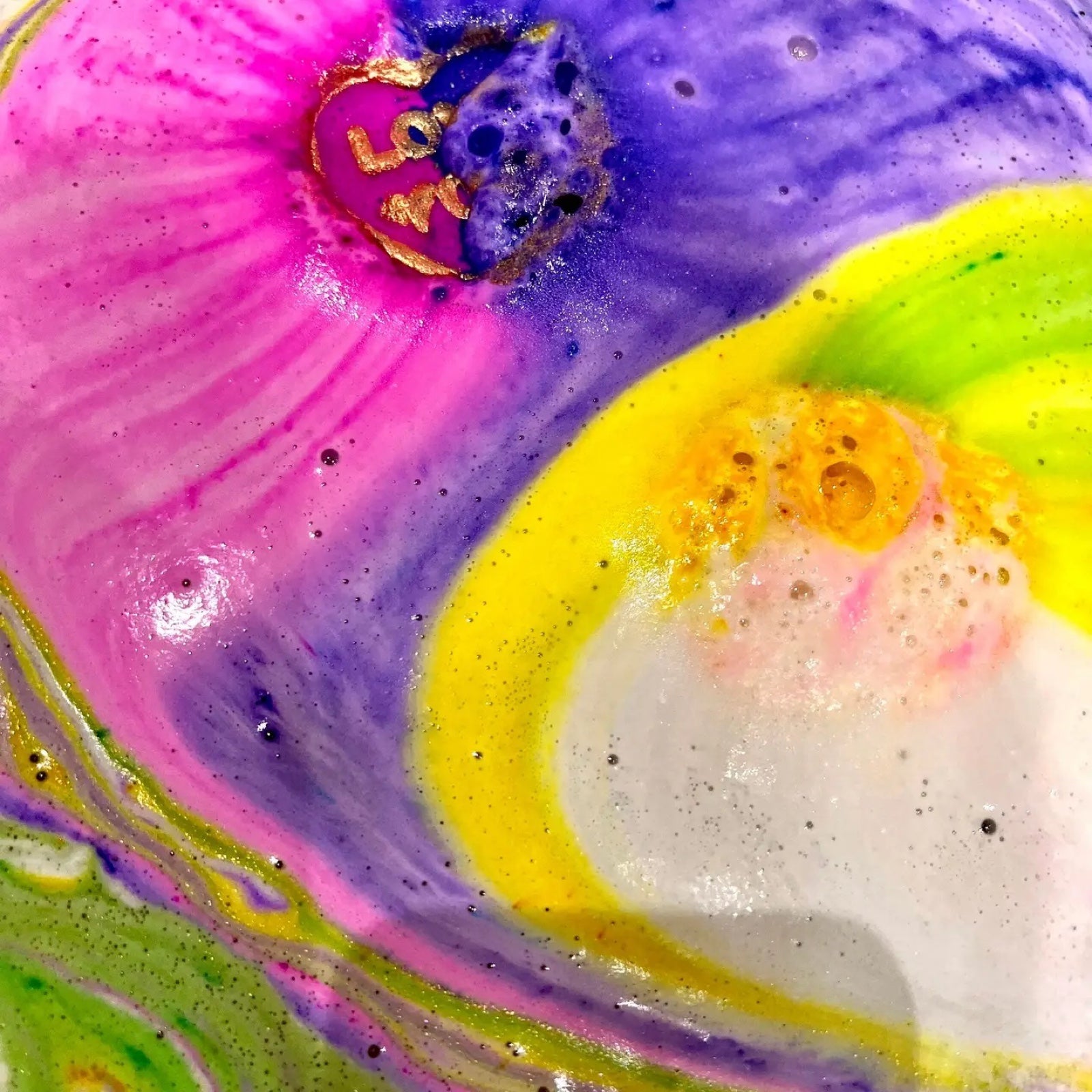 2 circular bath bombs inspired by the retro love heart sweets dissolving in the bath and turning the water pink, purple, yellow and green.