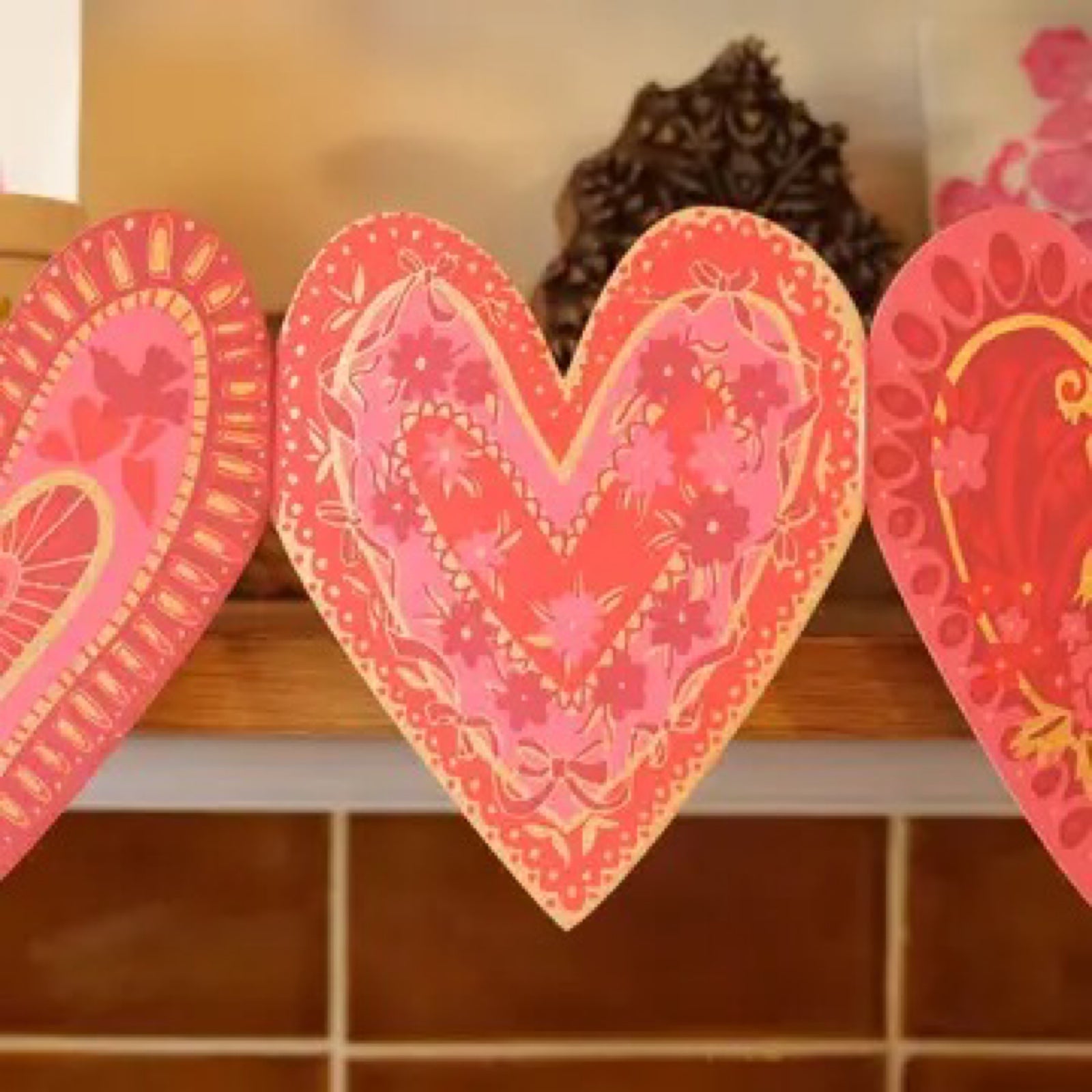 A red, pink and gold love heart-shaped concertina garland along a shelf edge.