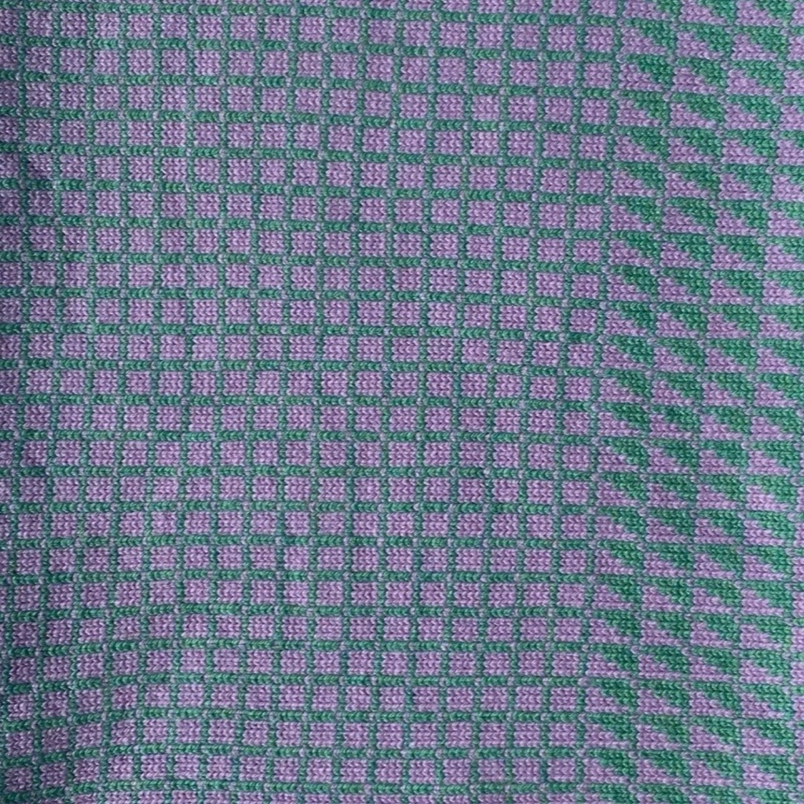 A close-up of a woven fabric with a repeating small check pattern in green and light purple, with a slightly denser border on the right side.