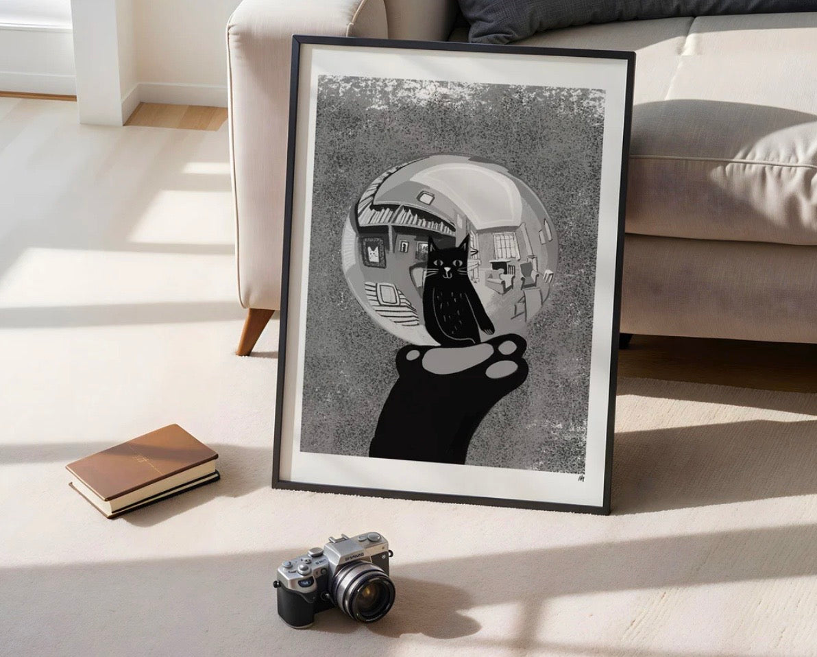 Framed black and white artwork of a cat in a bubble on a light-colored floor with a couch in the background.