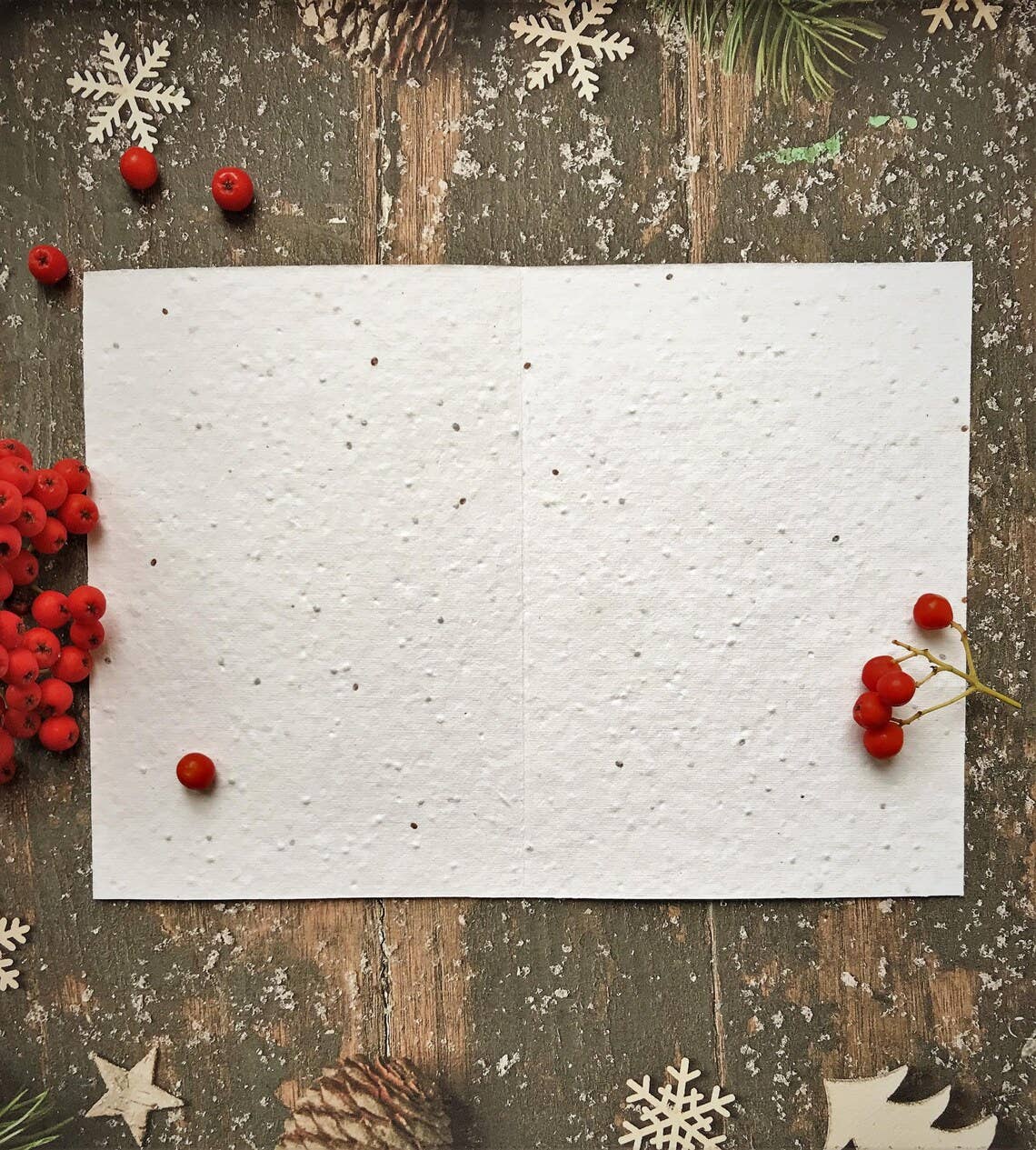 White textured paper on a rustic wooden surface with red berries and snowflake decorations.