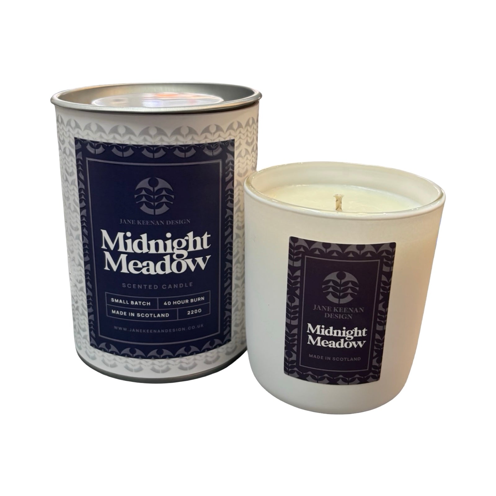 A candle next to its cylindrical metal tin packaging, both featuring a dark navy label with white text reading 'Midnight Meadow'.