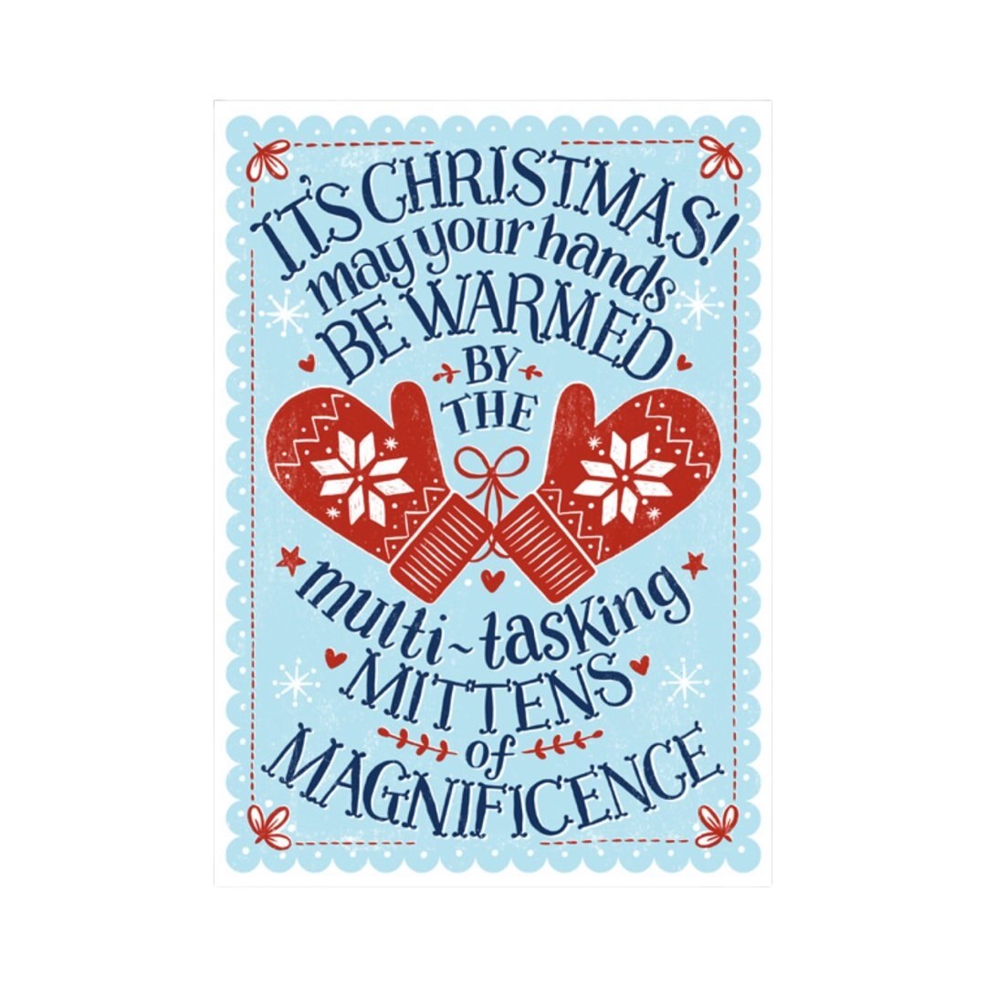 Christmas card featuring red woolly mittens with white flowers in the centre surrounded by the navy blue text It's Christmas! May your hands be warmed by the multi-tasking mittens of magnificence'. All on a pale blue background with a white border.
