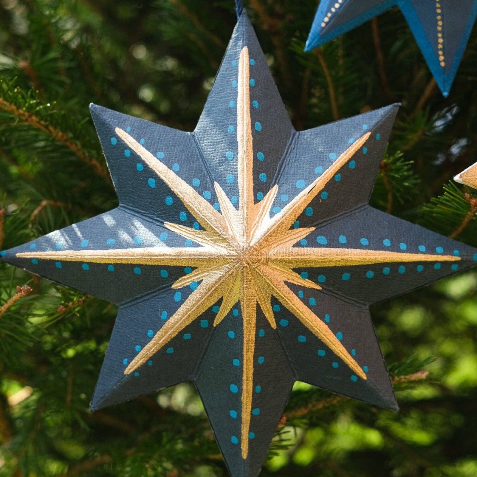 This festive navy, gold and teal star decoration has a matching 10cm cotton loop for hanging. Each star decoration is made from 100% recycled paper, screen-printed by hand and moulded into a durable board decoration.