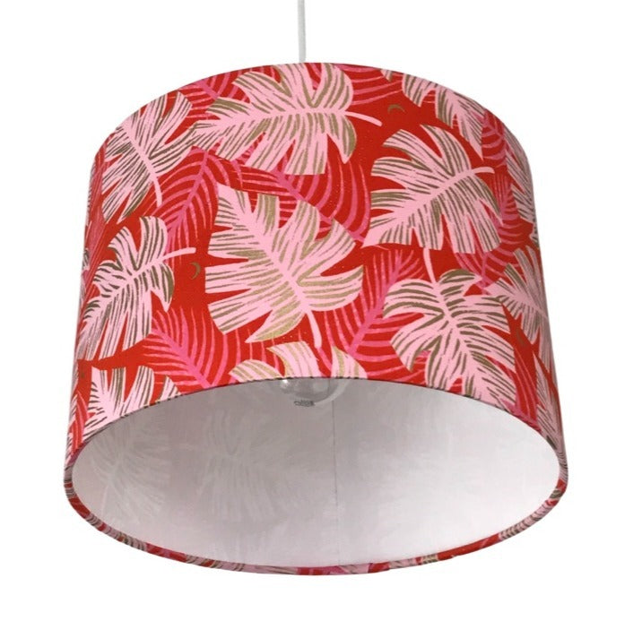 Drum lampshade covered in red cotton fabric with giant pink monstera leaves with gold details.