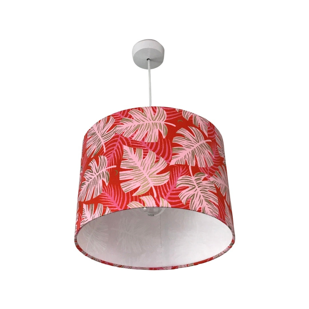 Drum lampshade covered in red cotton fabric with giant pink monstera leaves with gold details.