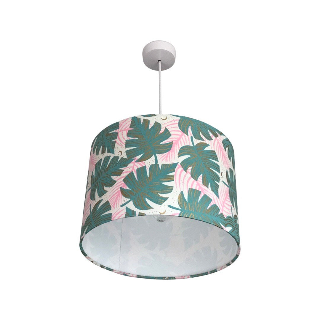 Drum lampshade covered in white fabric with green monstera leaves, pink leaves and gold detail.