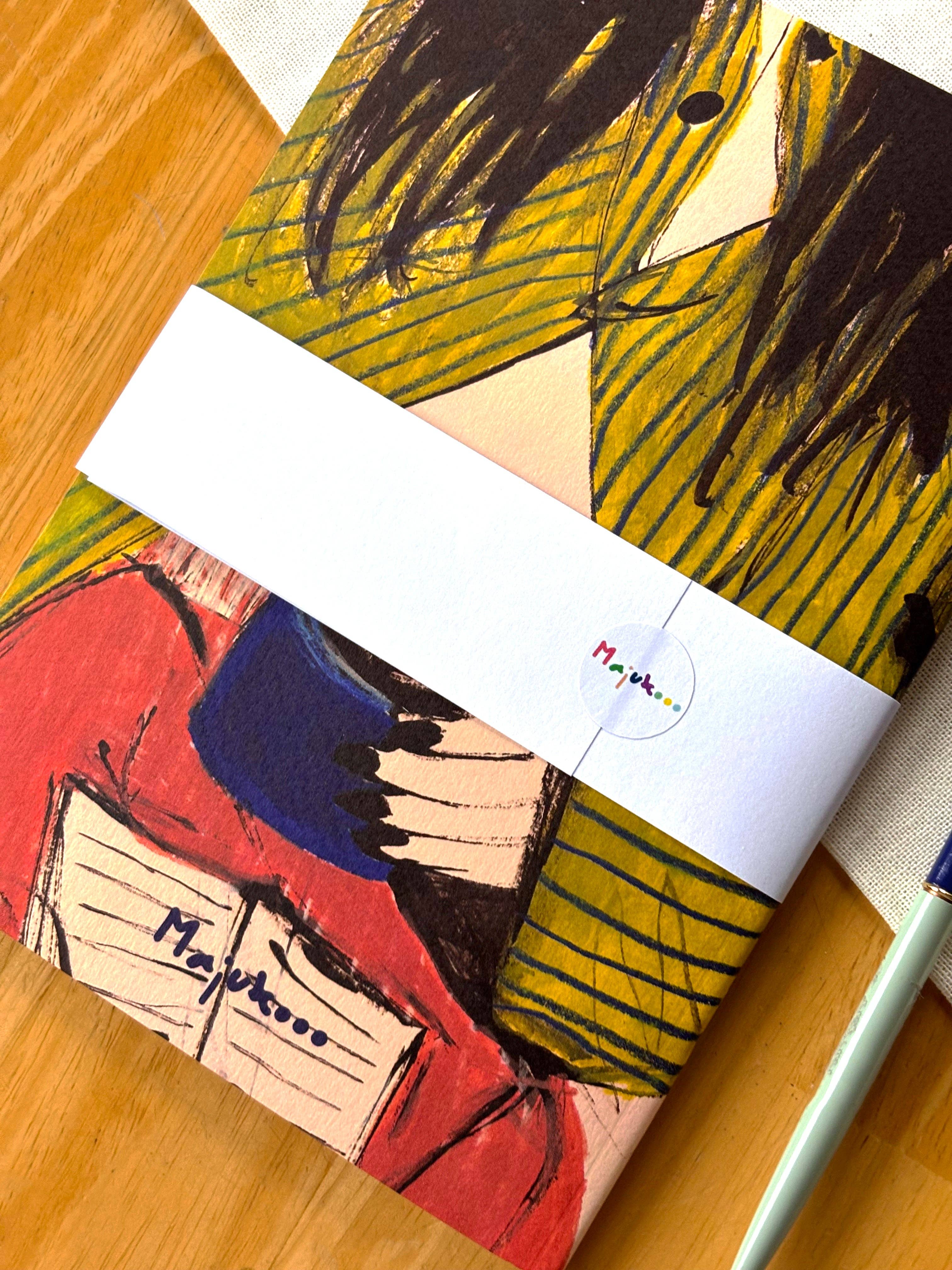 Notebook with artistic cover and Majukooo logo on a wooden surface.