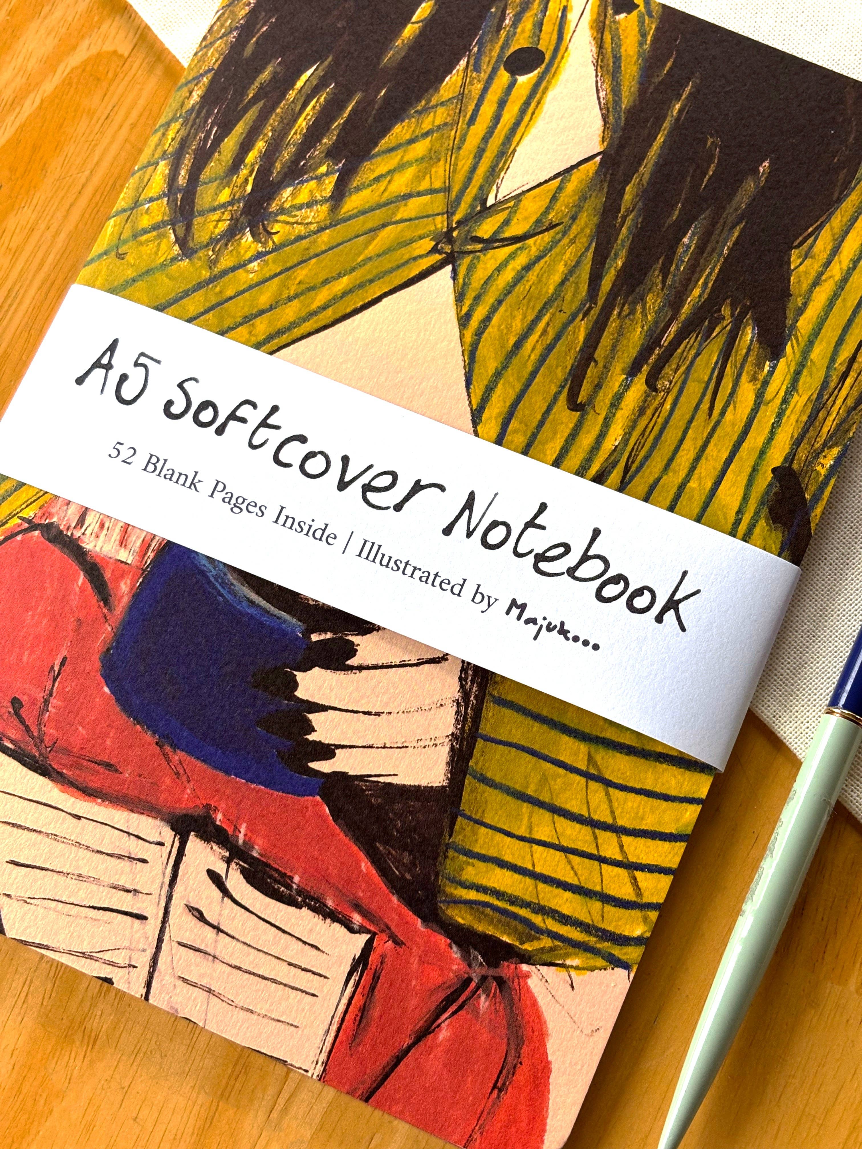A5 softcover notebook with colorful illustrations and a pen on a wooden surface.