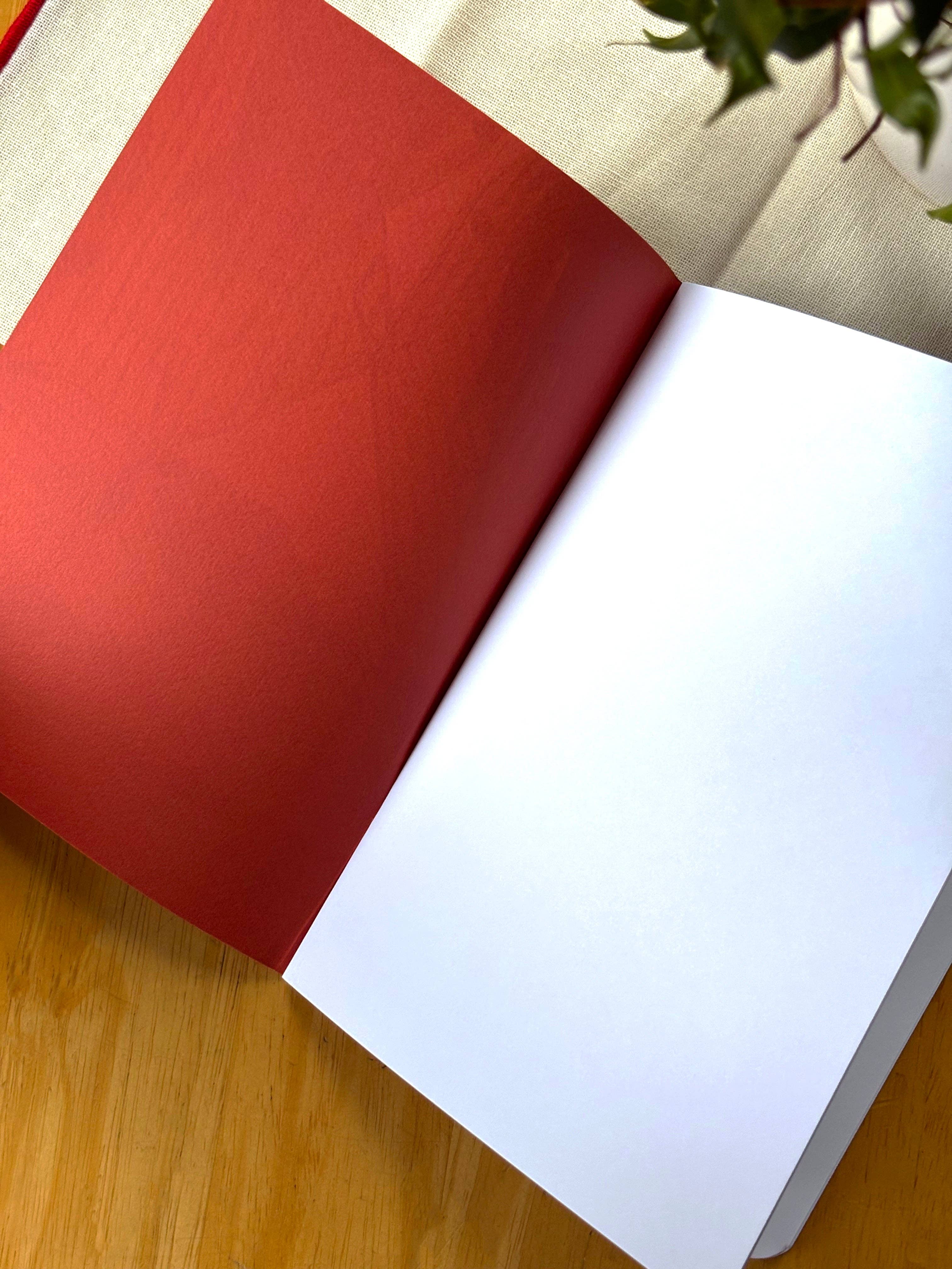 Open book with red cover and white pages on a wooden surface.