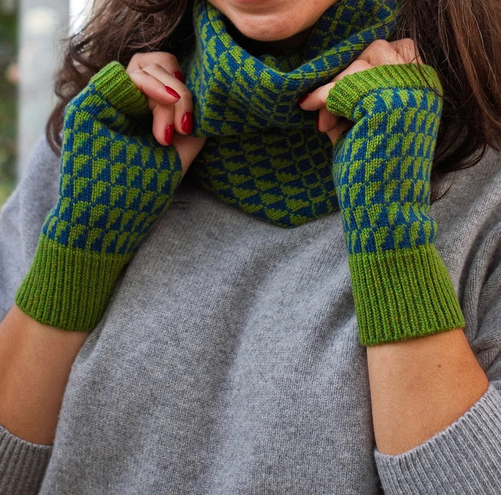 Person wearing green patterned wrist warmers and snood with a blurred background.