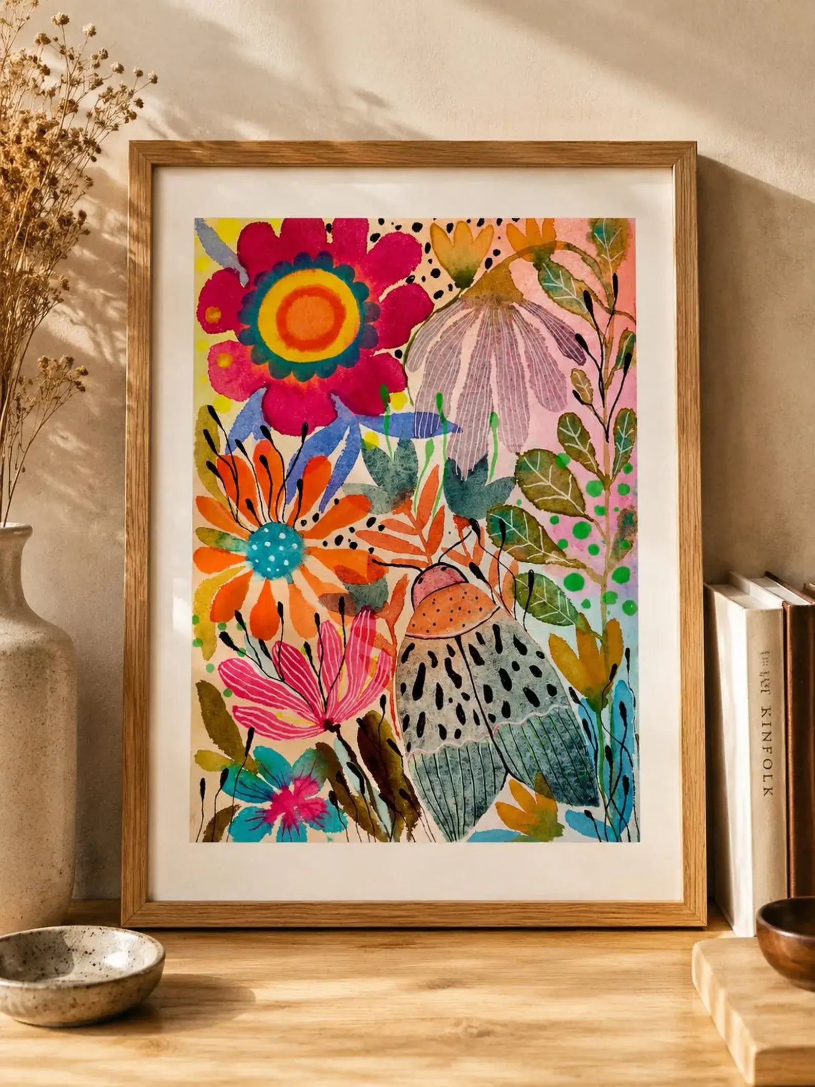 Framed colourful floral artwork on a wooden surface with books and decor items.