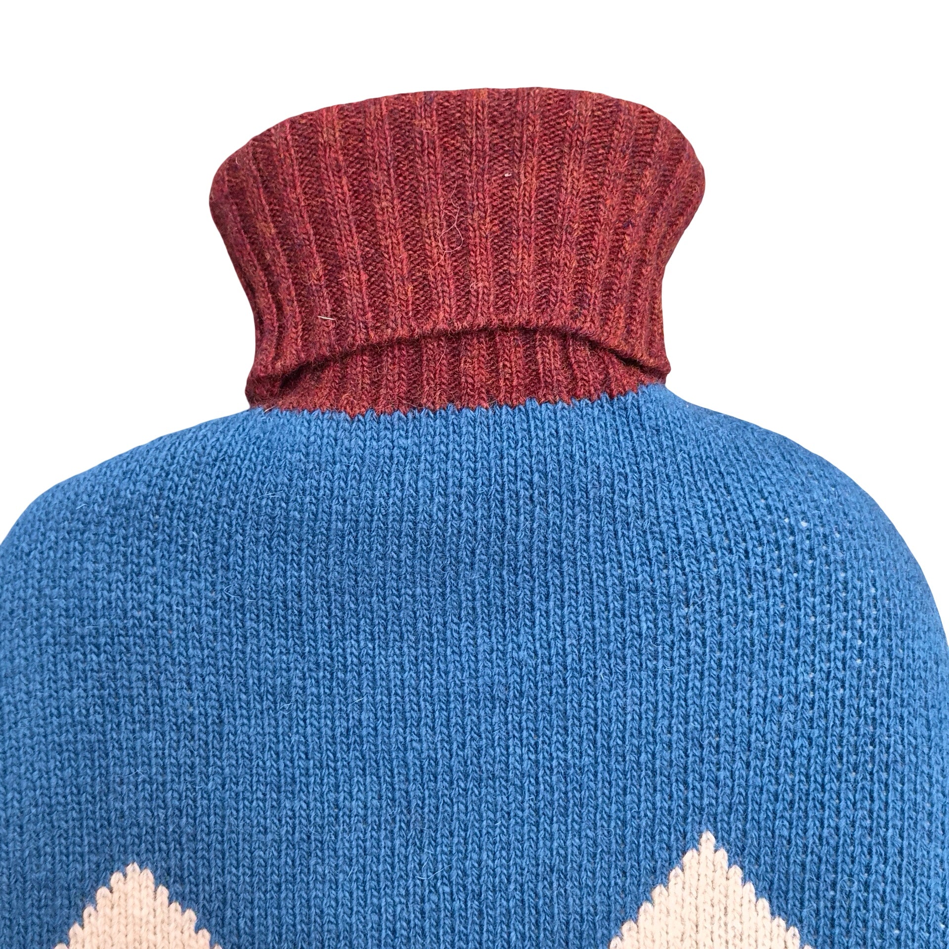 Close-up of a knit turtleneck hot water bottle showing a ribbed burgundy collar and a blue body with cream geometric patterns at the bottom, on a white background.