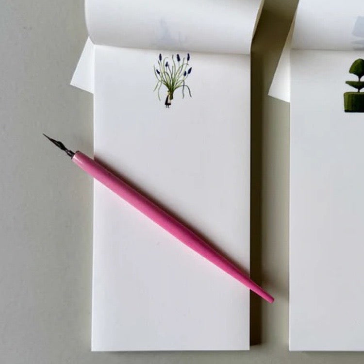 White notepads with plant designs and a pink pen on a light grey background.