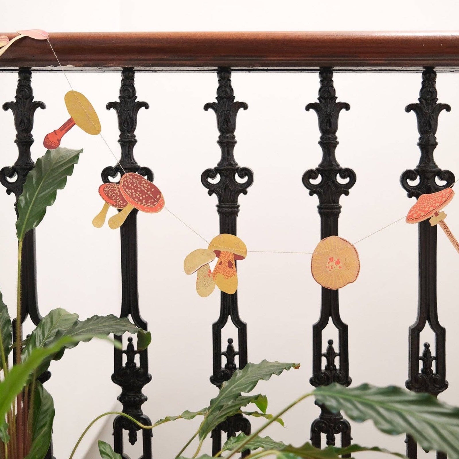 A paper garland featuring twenty screen-printed mushrooms and toadstools in red, gold and orange designs hanging along a black metal bannister.