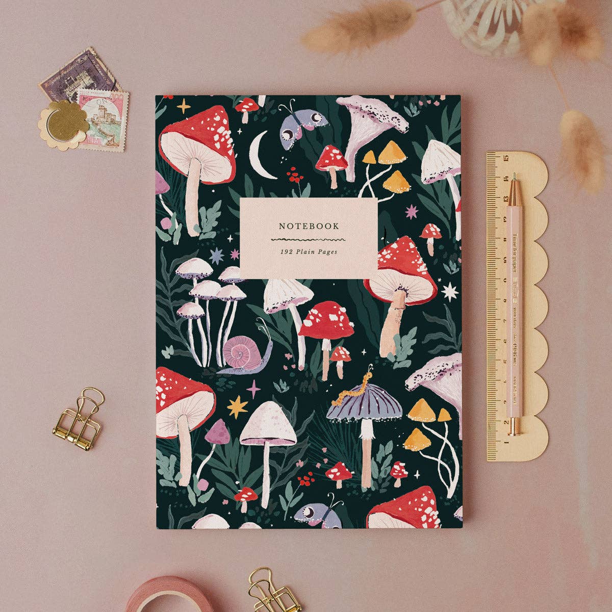 Notebook with mushroom design on a pink background with stationery items.