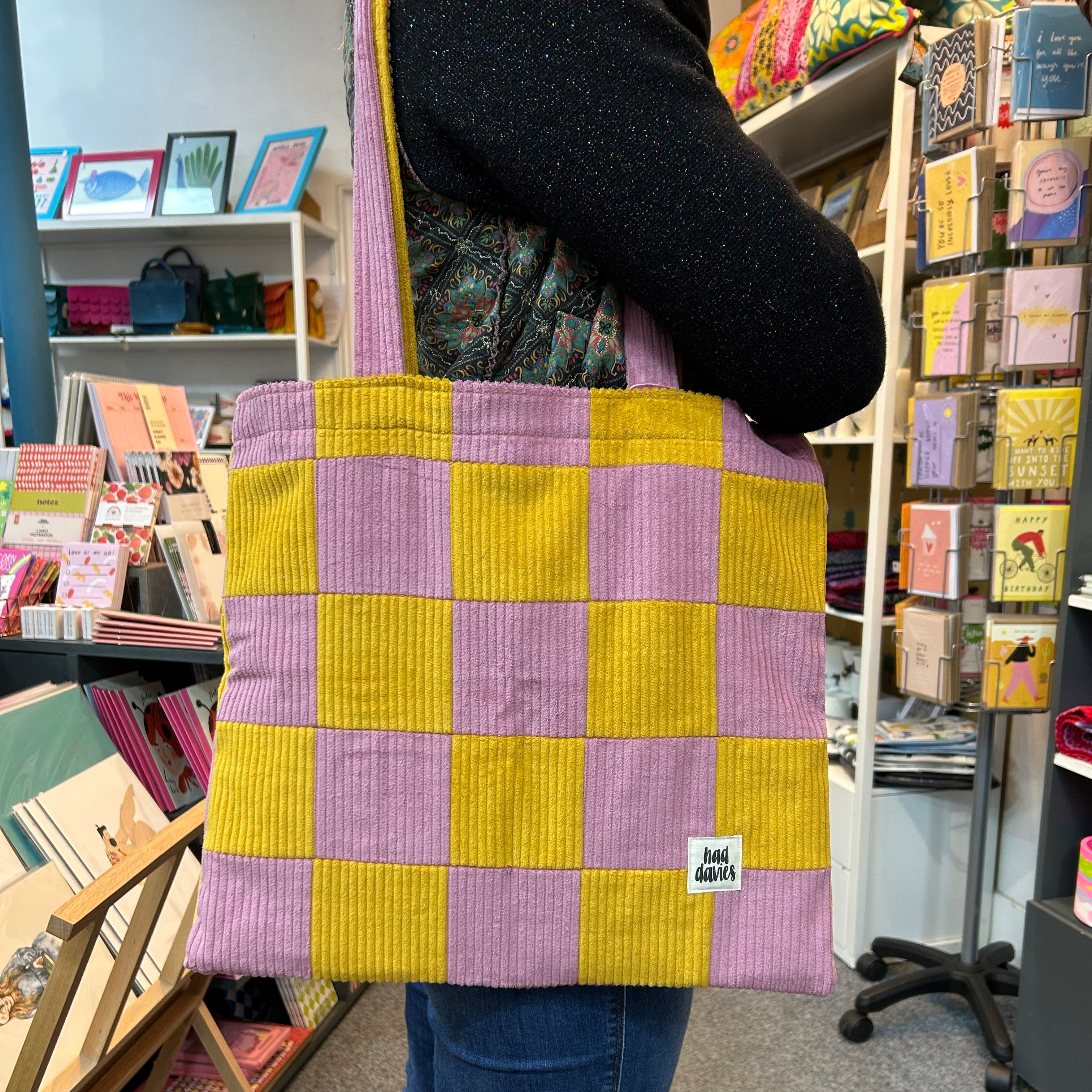 Person holding a checkered purple and yellow bag in a store setting.