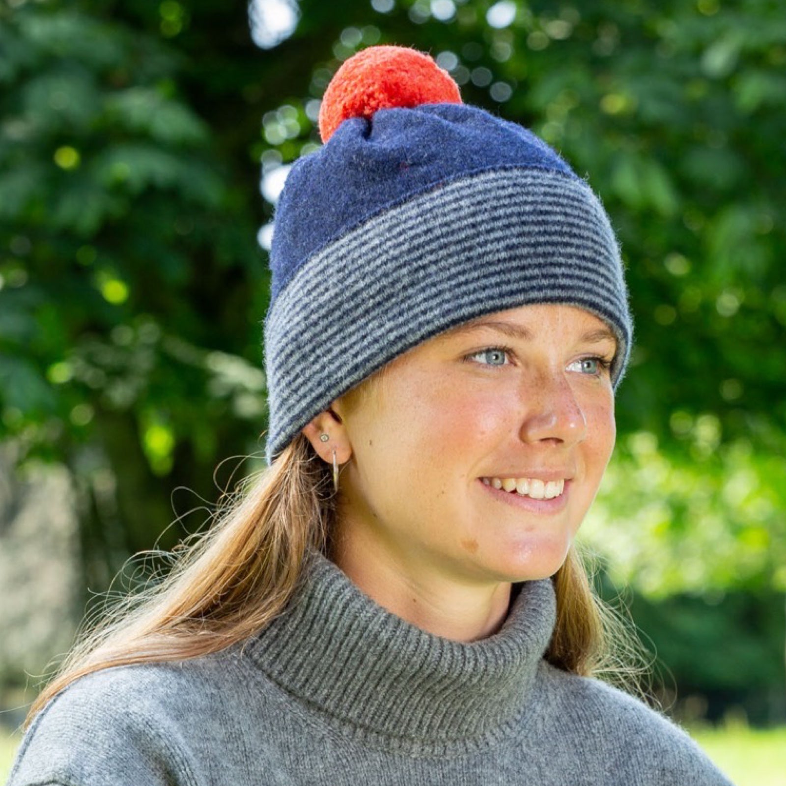 Person wearing a blue and gray striped beanie with an orange pom-pom.