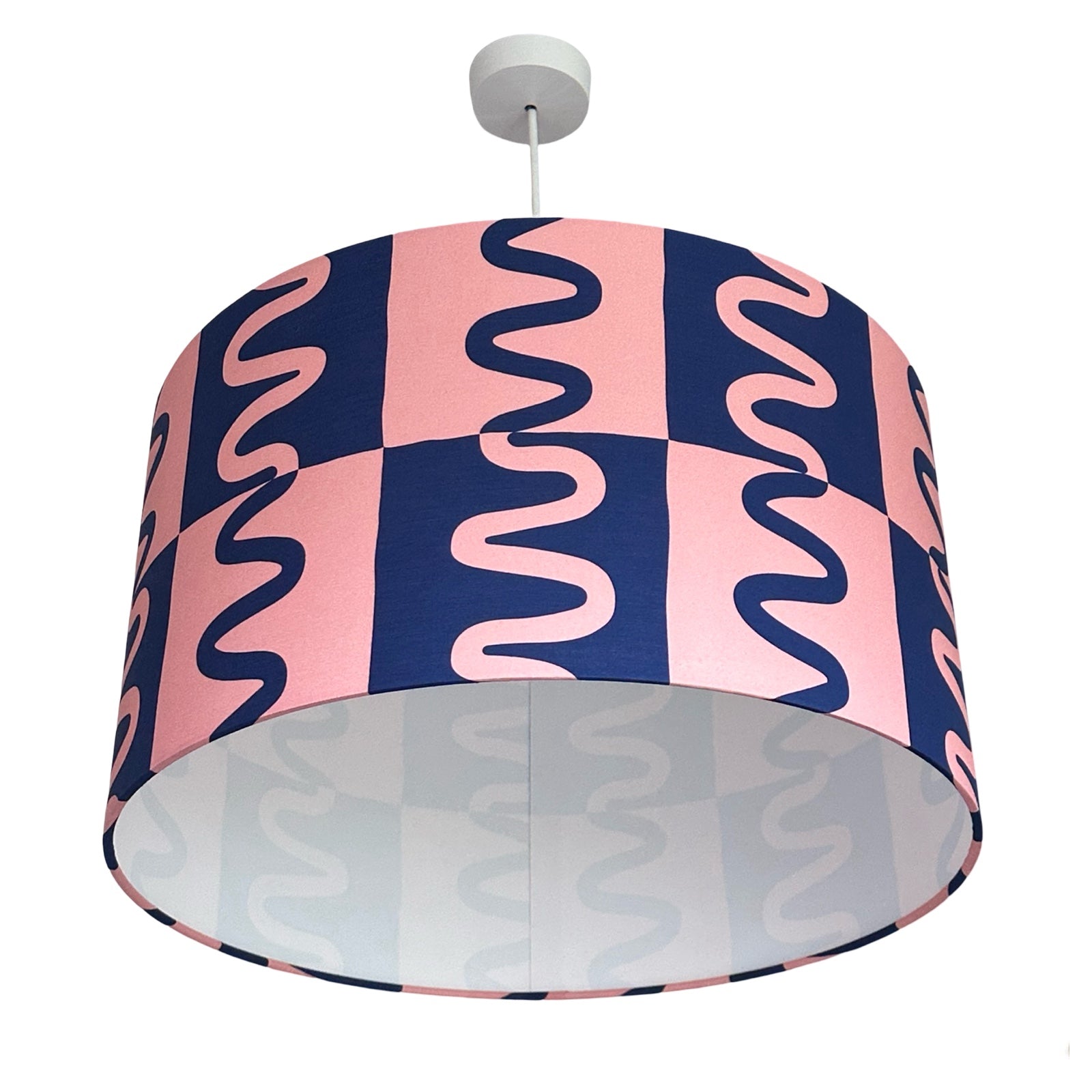 A drum lampshade covered in striking pink and blue cotton fabric with squiggles running through contrasting squares.