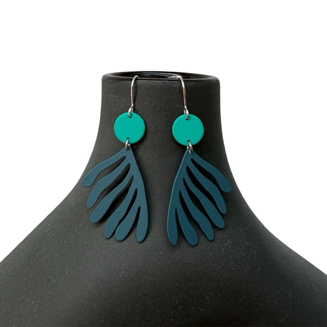 Teal and blue earrings on a black mannequin against a white background.