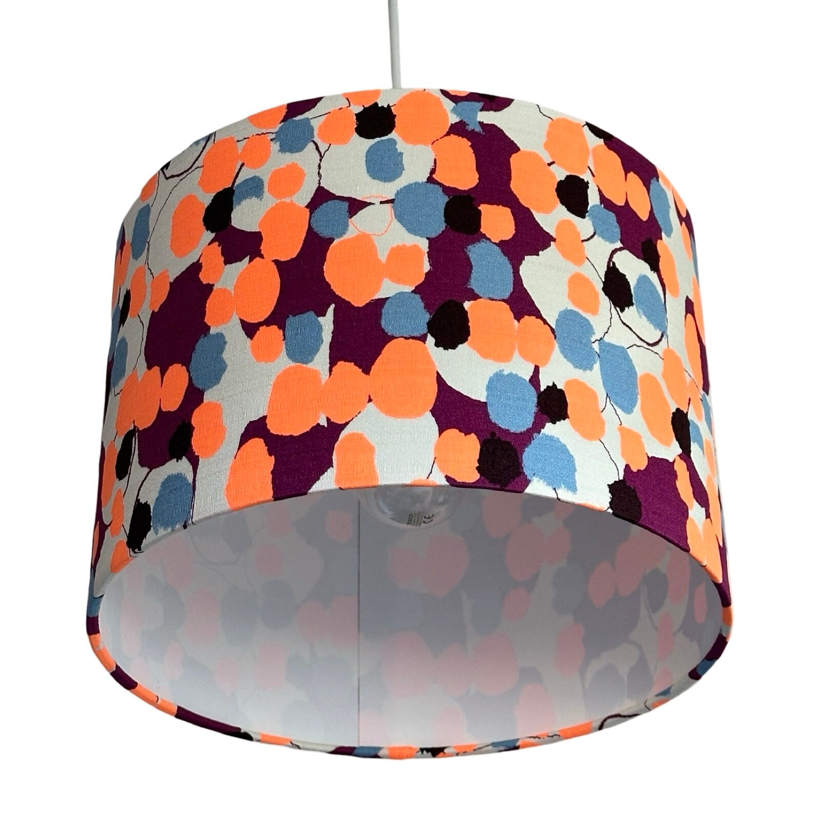 Handmade drum lampshade covered in barkcloth fabric with neon orange and blue blossoms on a purple and cream background.