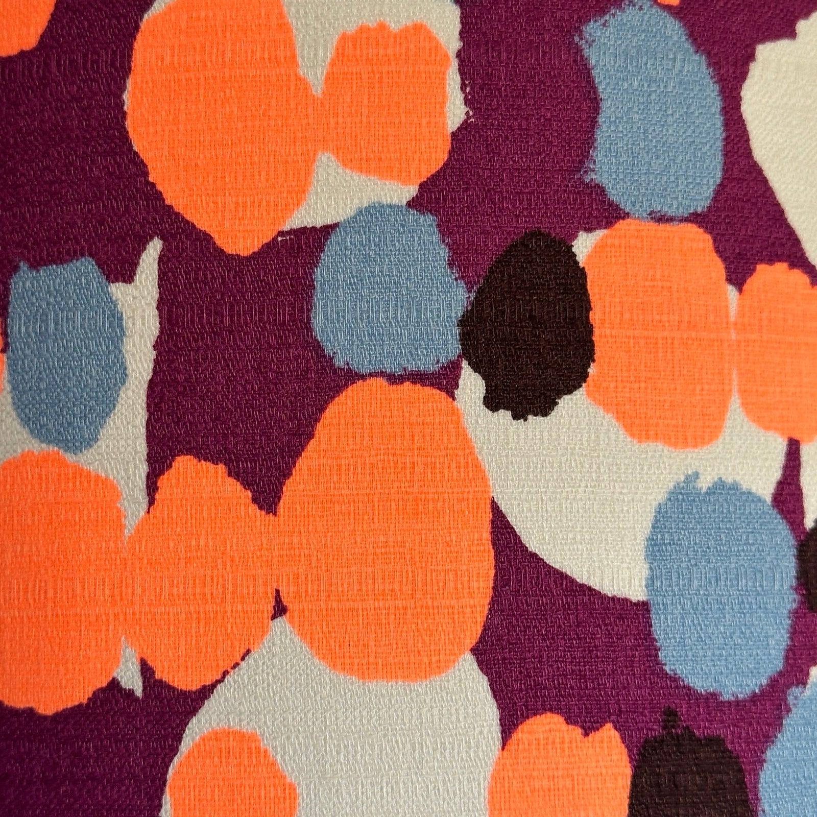 barkcloth fabric with neon orange and blue blossoms on a purple and cream background.