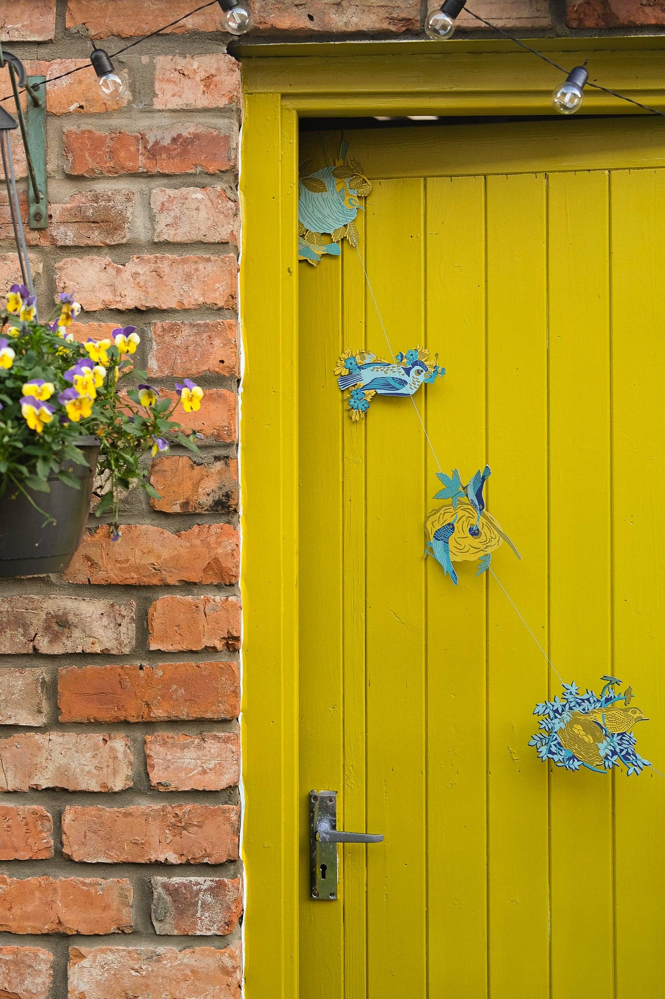 This beautiful nest garland features ten screen-printed bird nests full of speckled eggs, flowers and twigs, on a yellow door.