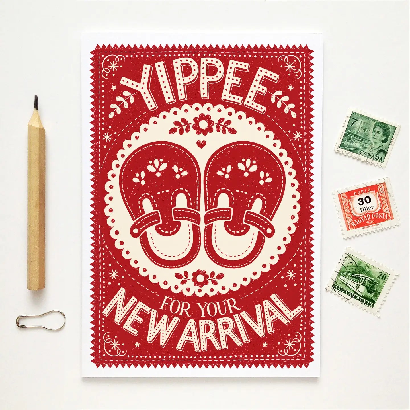 Red and white baby shower card with 'Yippee for your new arrival' text, surrounded by vintage stamps and a pencil on a white background.