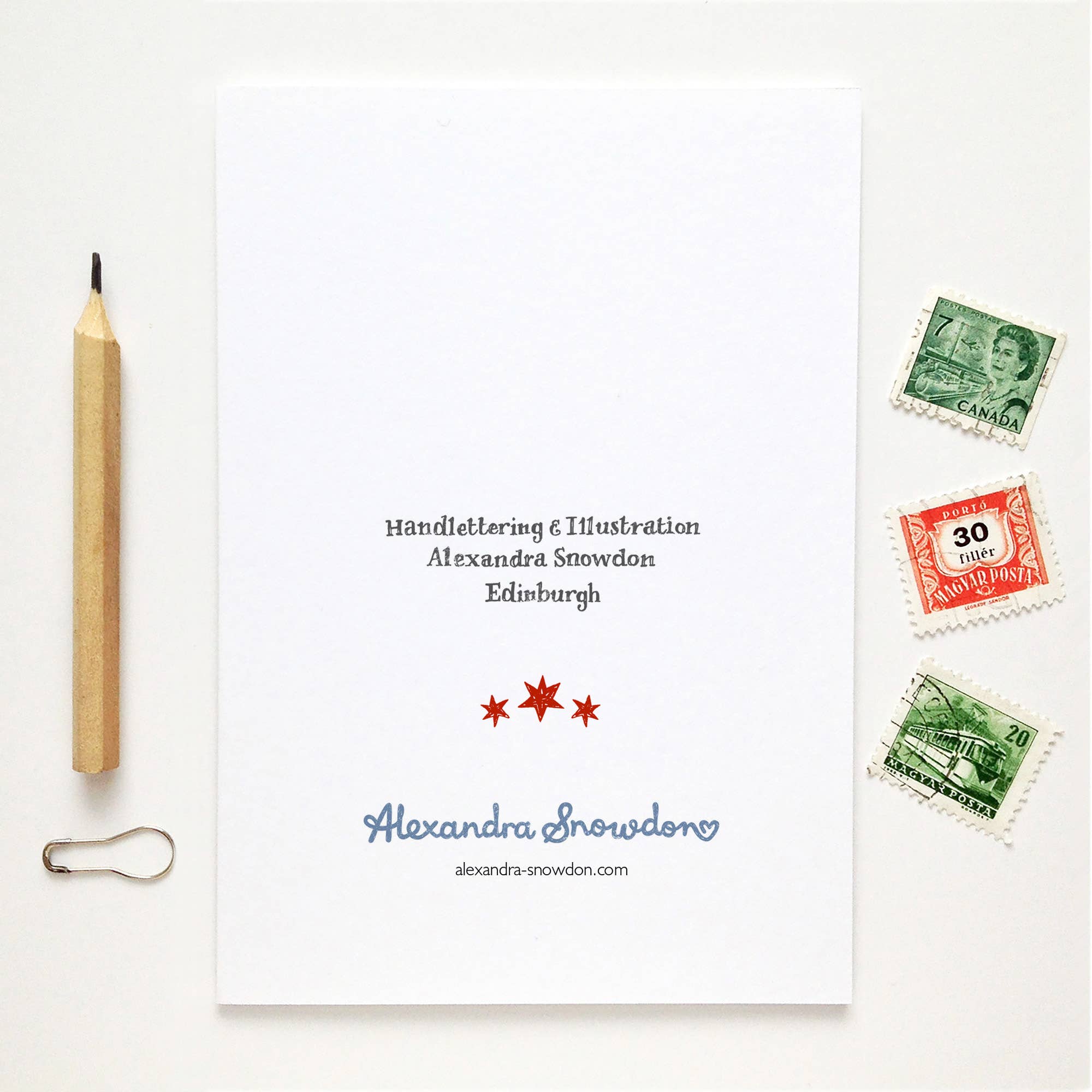 Note card with stamps, pencil, and paper clip on a white background.