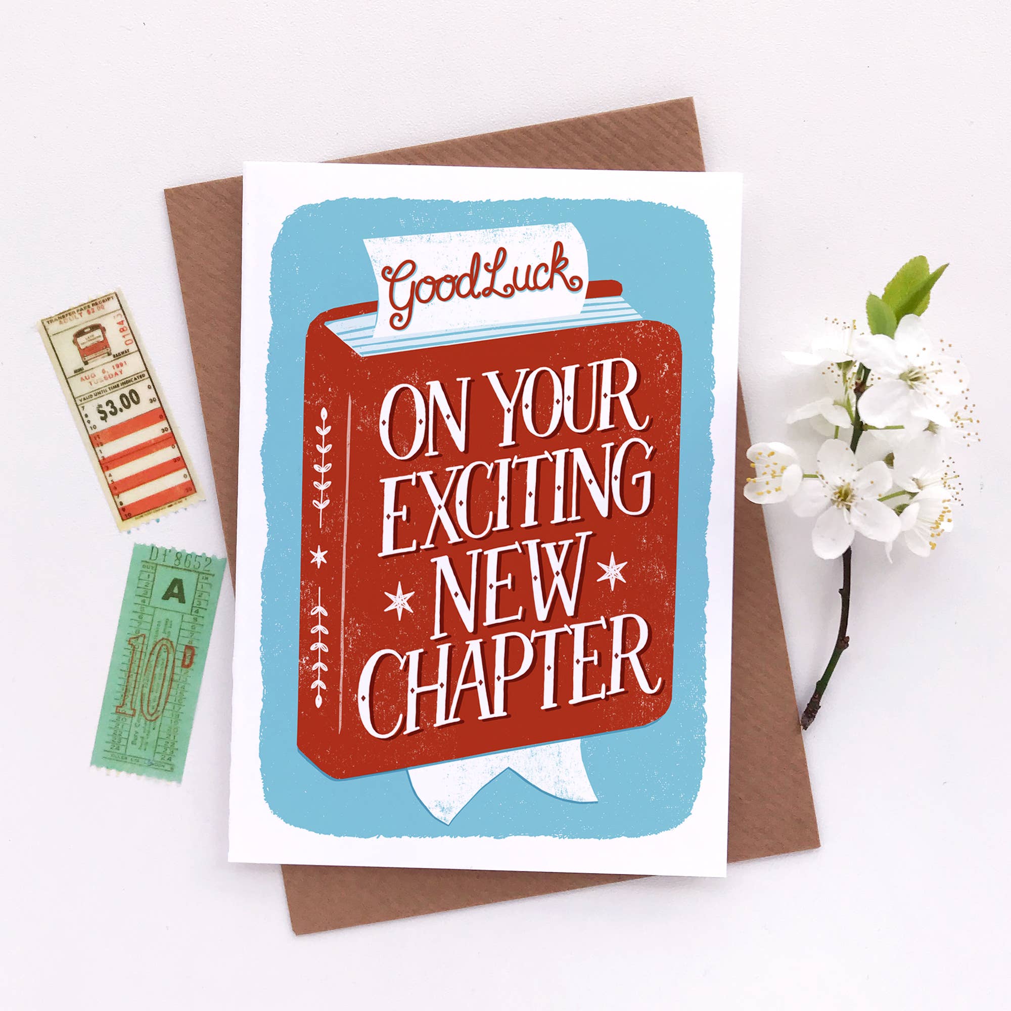 Greeting card with 'Good Luck on Your Exciting New Chapter' text, bookmark, and tickets on a white background.