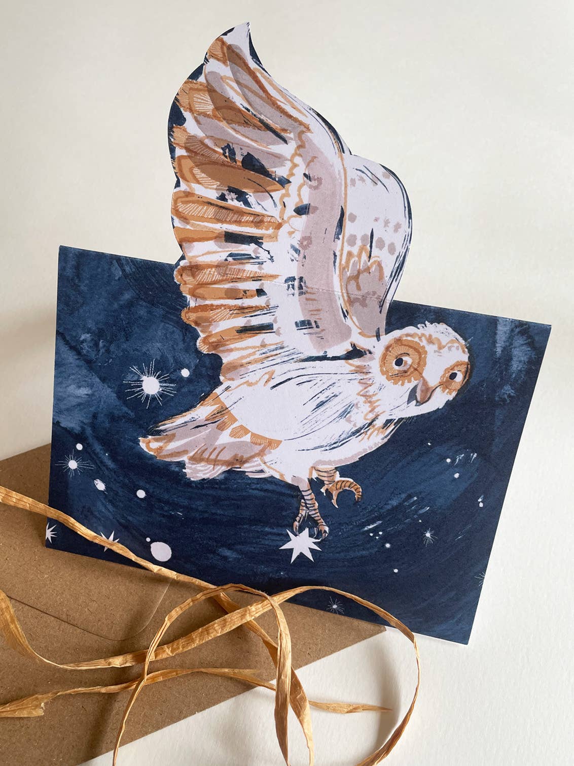 Greeting card with an owl design on a starry night background, accompanied by a brown envelope.