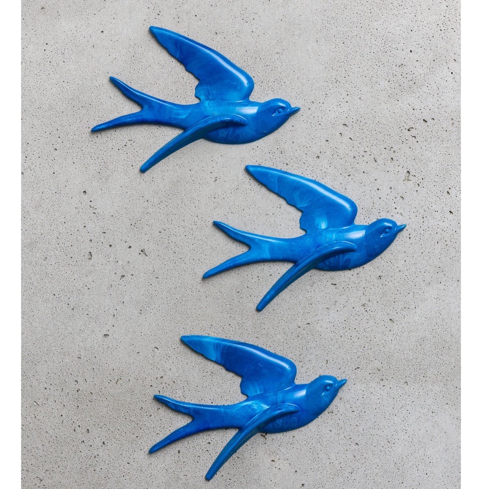 Three blue bird-shaped sculptures on a grey concrete surface.