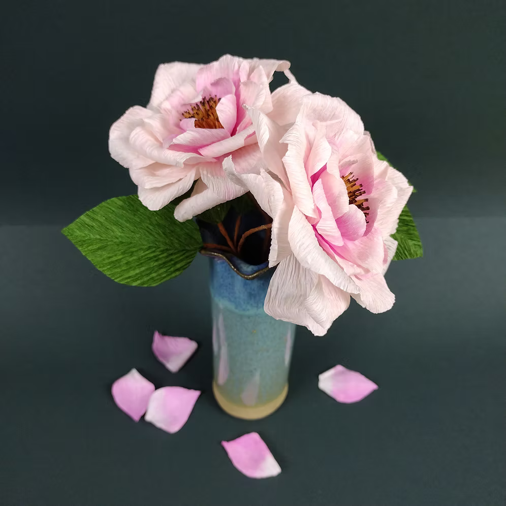 Pink flowers in a vase with scattered petals on a dark background.