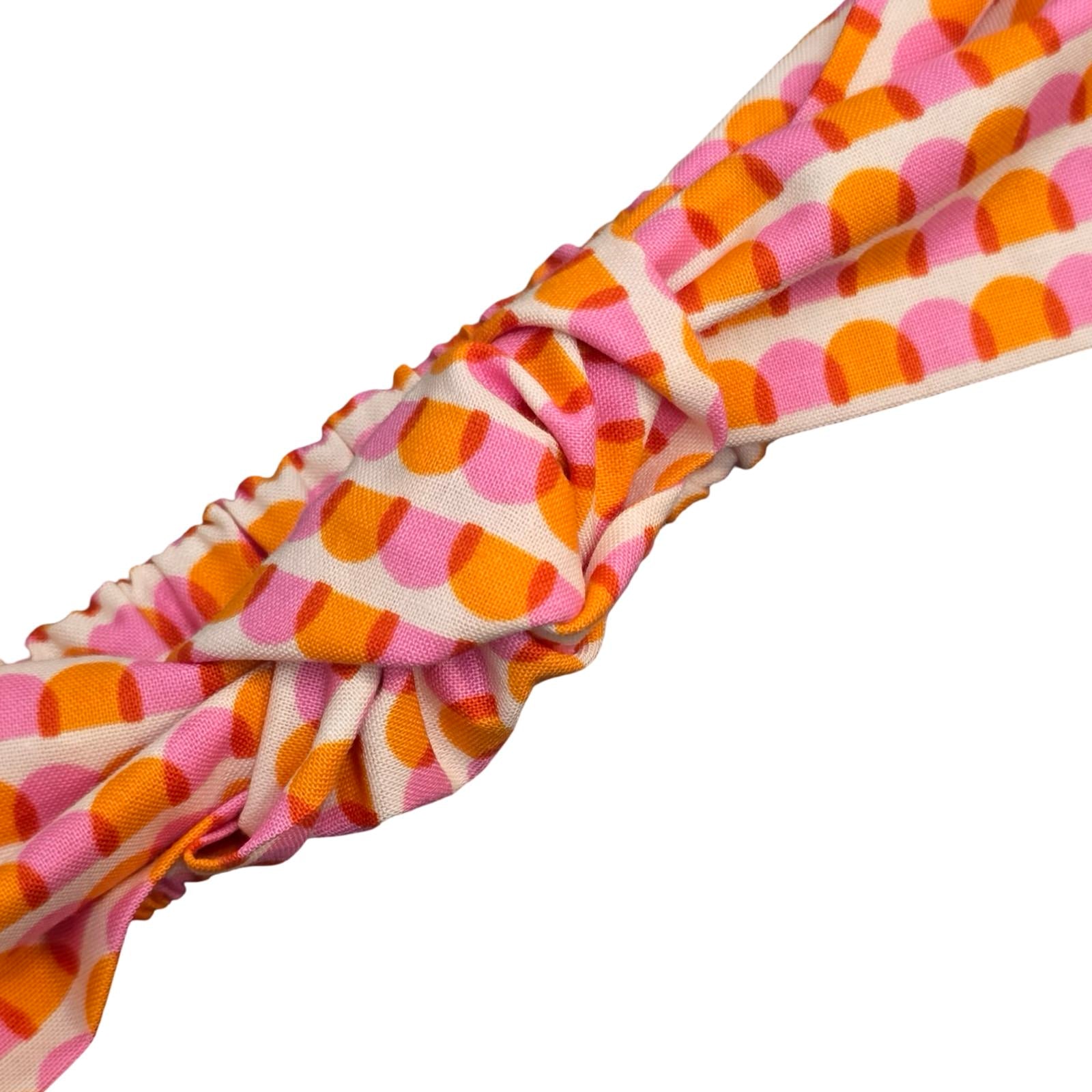 This handmade knotted headband is made from 100% cotton fabric with an orange and pink scalloped pattern.