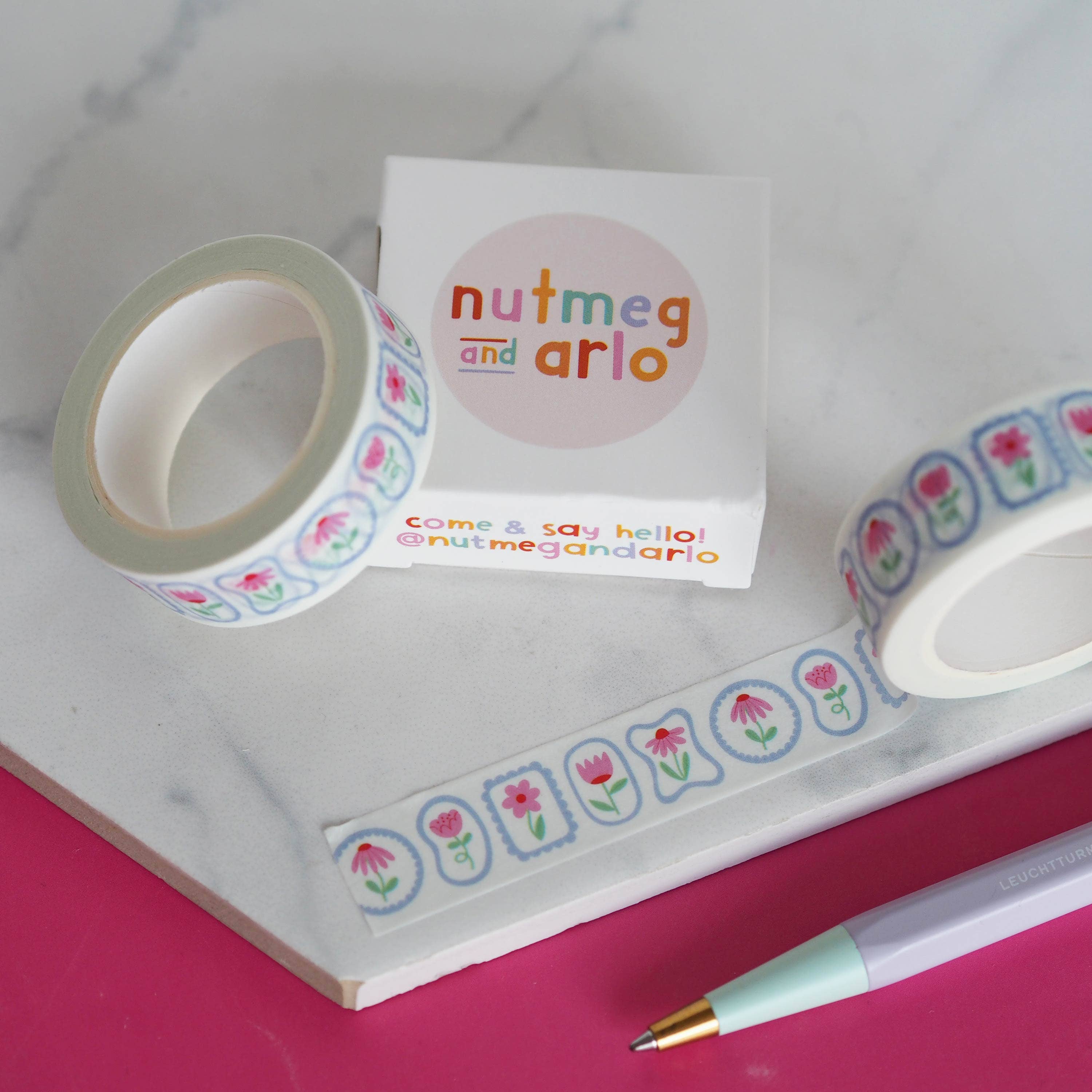 Decorative tape with floral designs and a 'nutmeg and arlo' label on a pink surface.