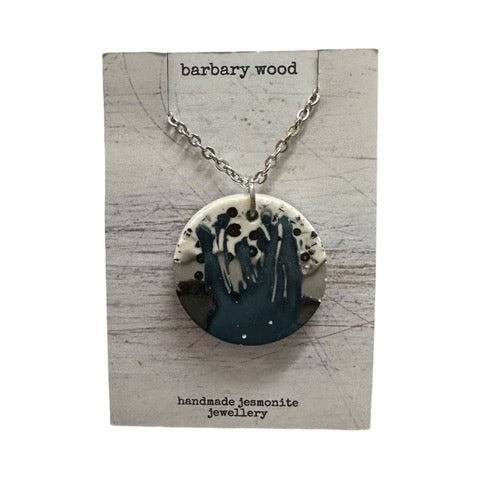 A circular pendant necklace with a blue, black, grey and white design on a silver chain.