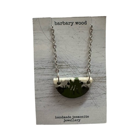 A green half moon necklace with a black and white abstract design on a silver chain.