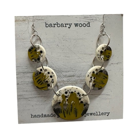 Necklace with 5 mustard circular pendants with a black, grey and white paint design held together with silver findings.